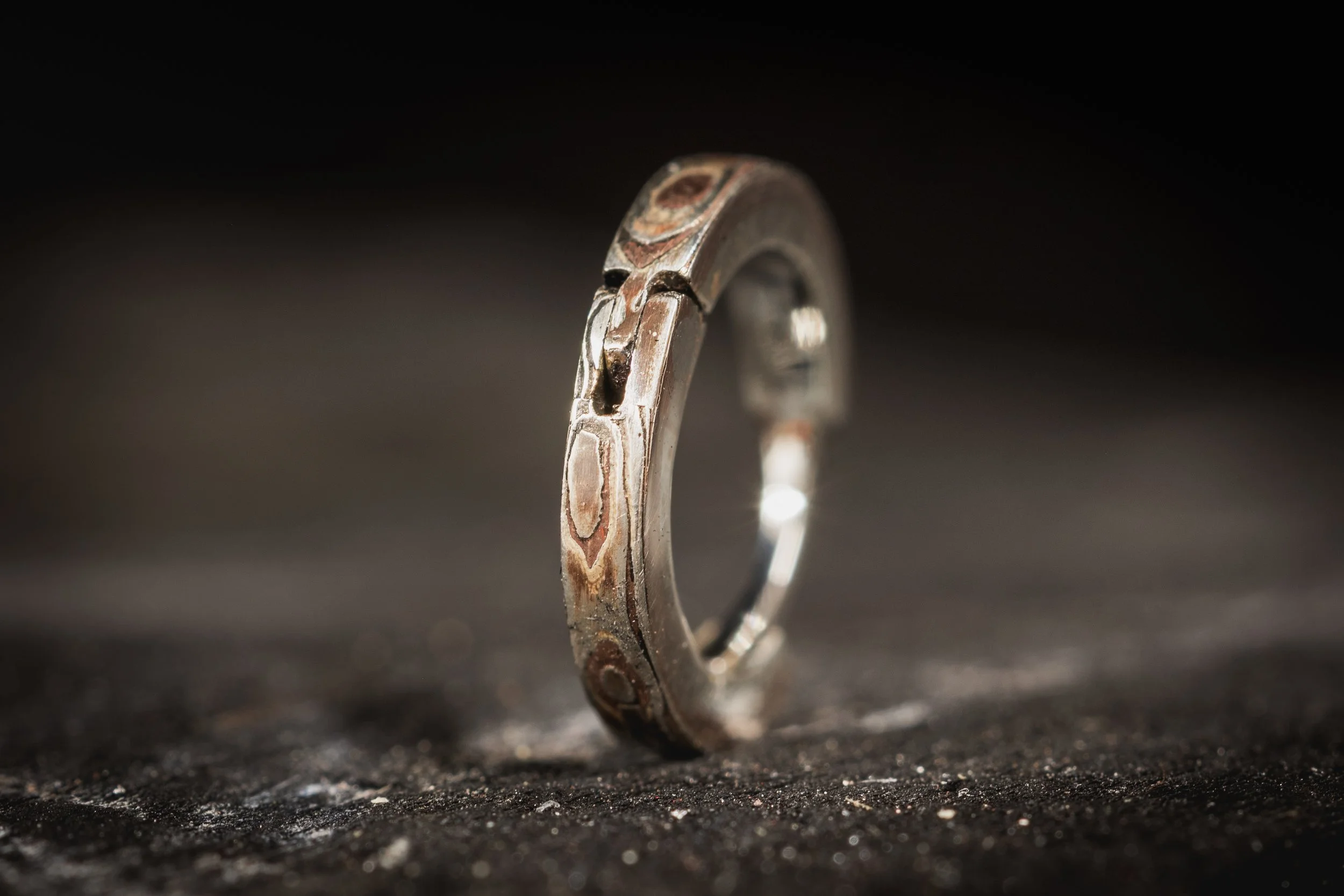 Close-up of a metallic ring standing upright on a dark, textured surface with a black background.