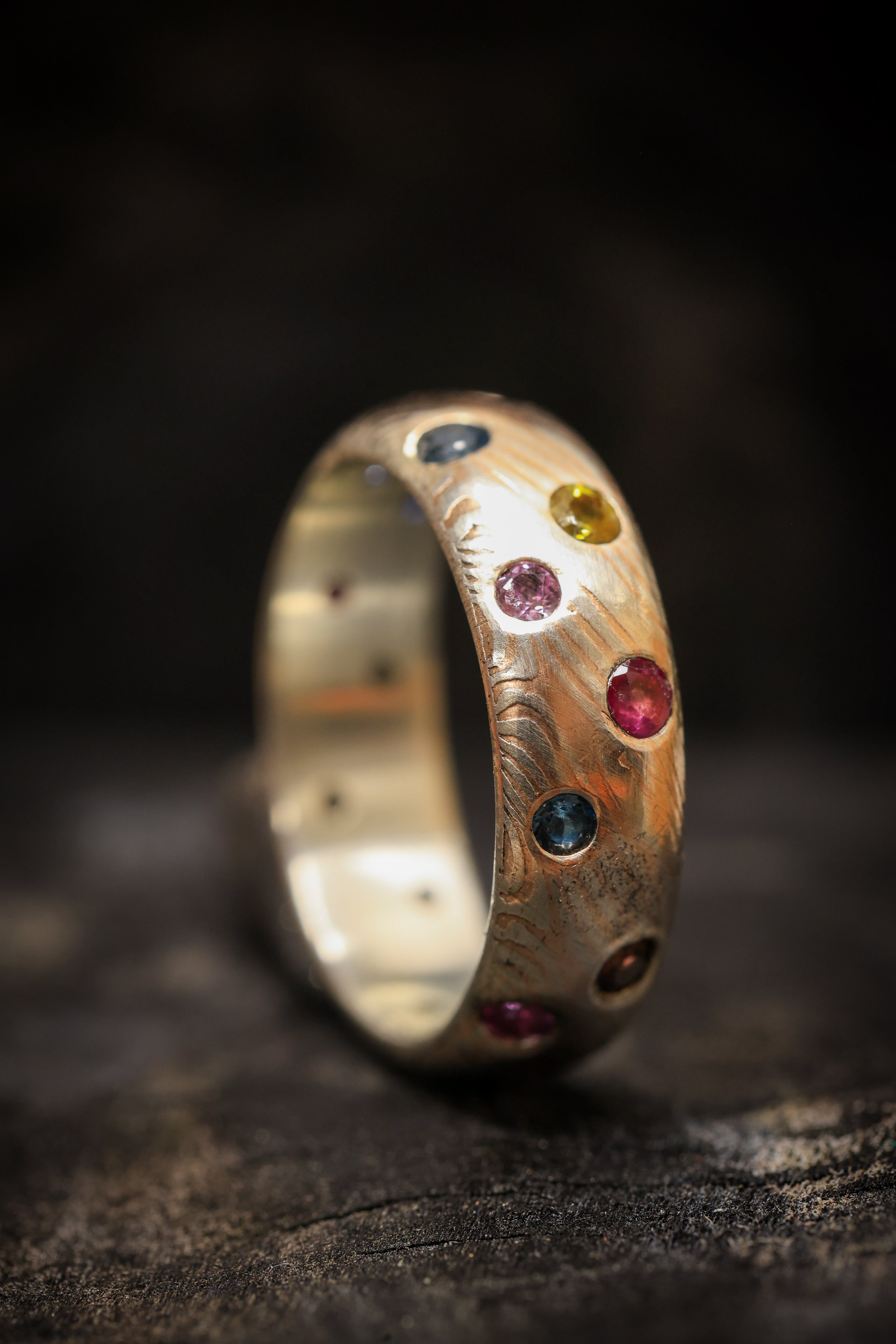 Close-up of a gold ring with embedded multicolored gemstones, resting on a dark surface.