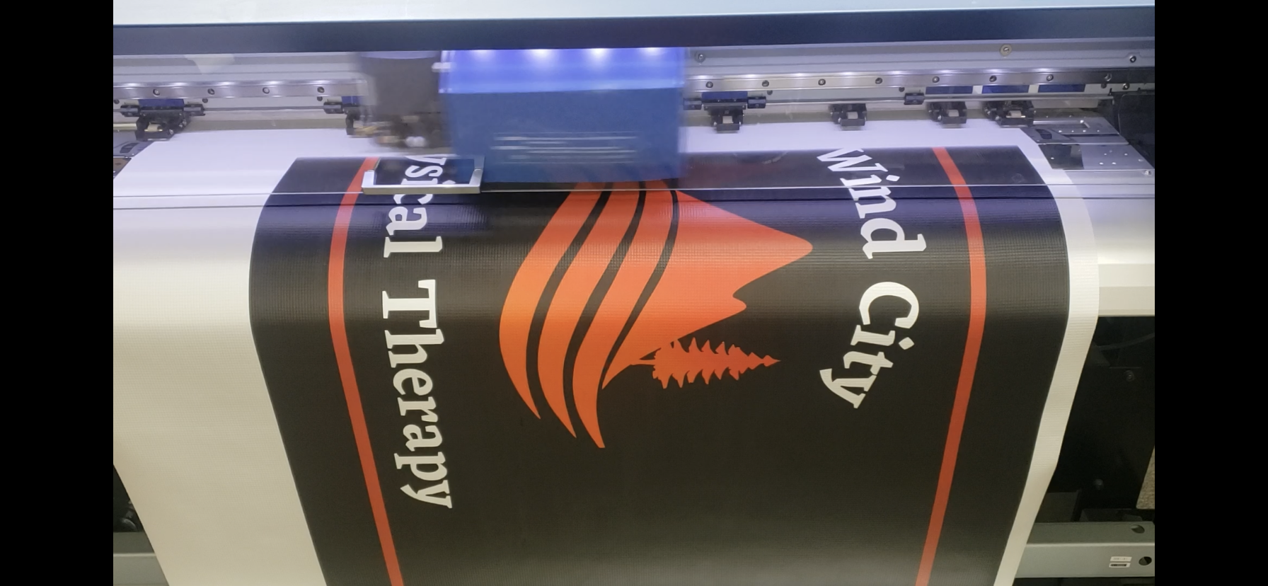 A printing machine printing a banner, with a part of the machine visible at the top and bottom.