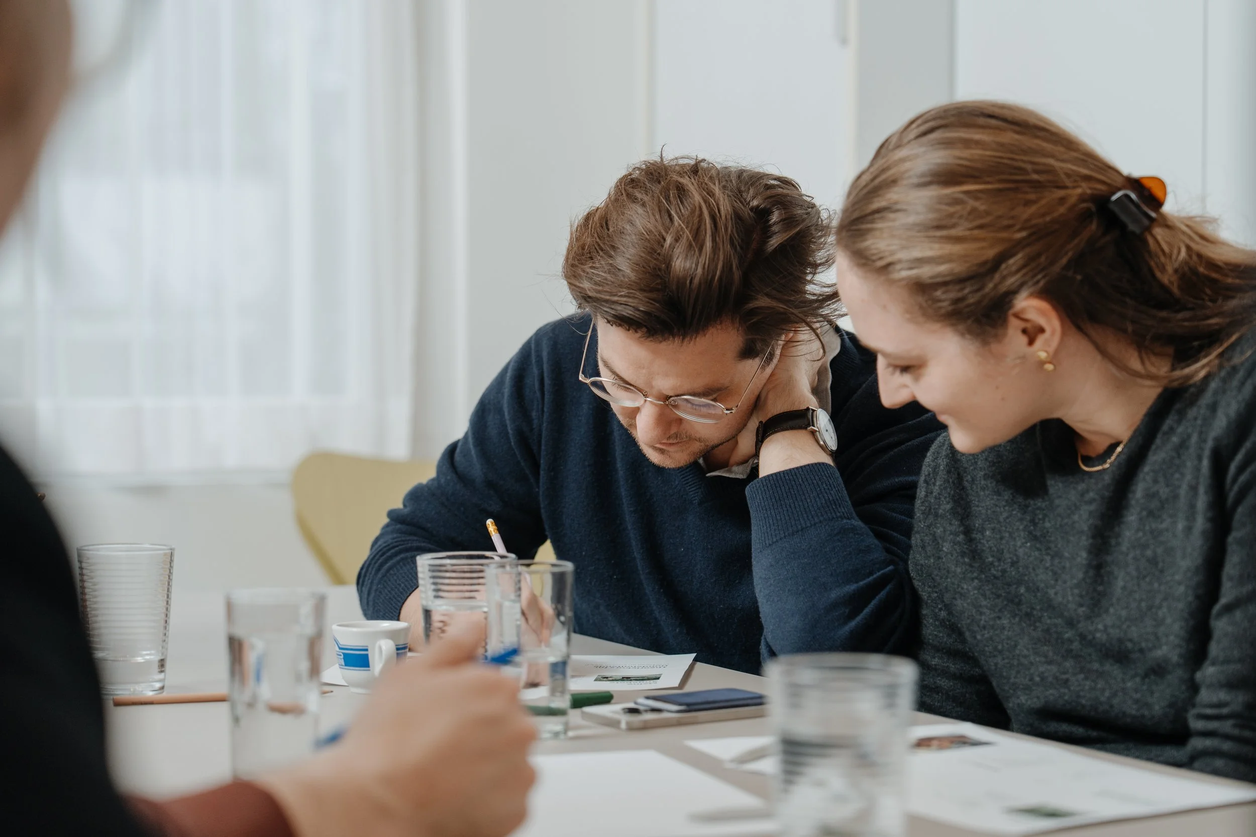 Zwei Teilnehmende schauen auf die ausgedruckte Präsentation beim Kurs und besprechen etwas, mit Wasser und Kaffee auf dem Tisch.