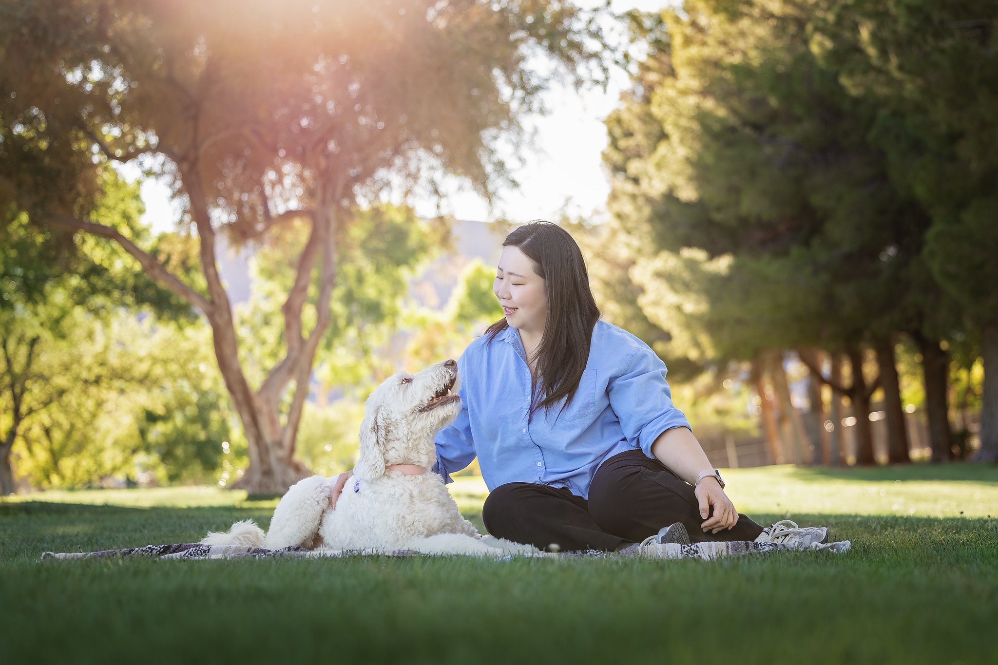 woman sitting in the grass at the park with her white doogle dog