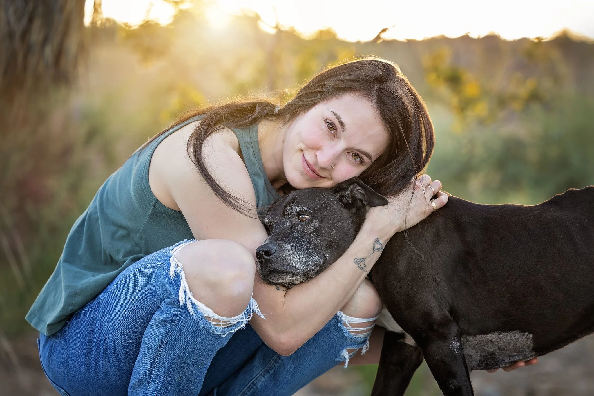 woman hugging her black pitbull mix at sunset
