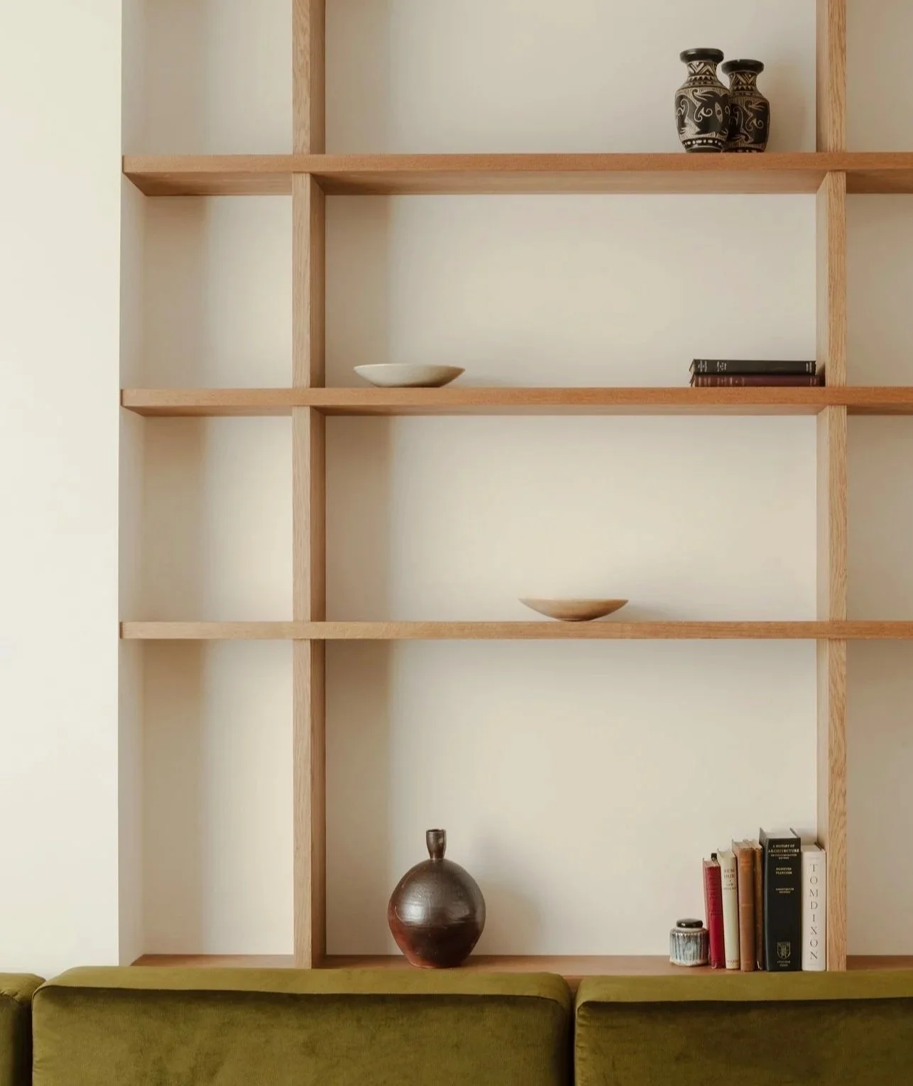 Empty wooden bookshelf with decorative vases, books, and bowls, and a green sofa in front.