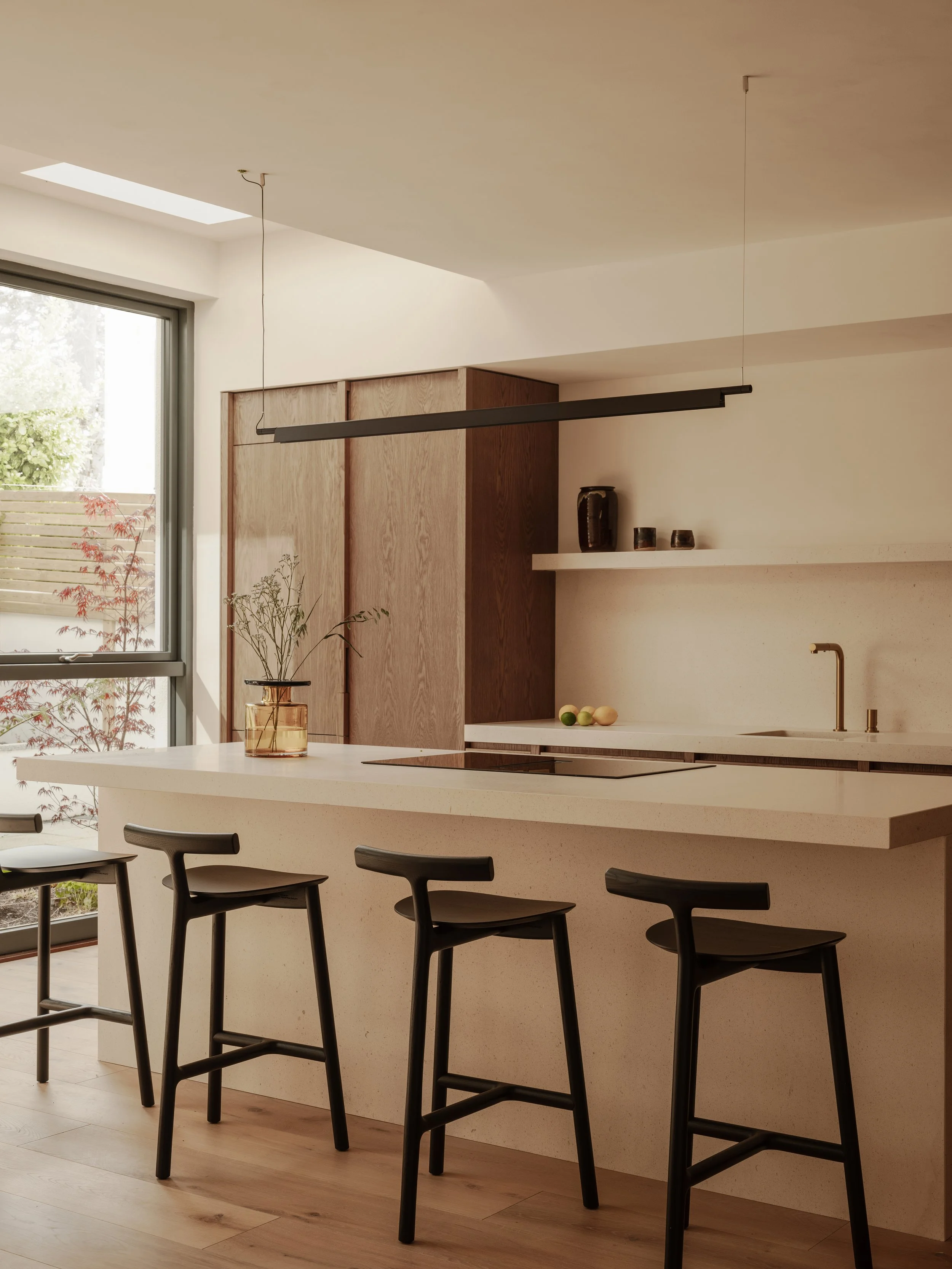 Modern kitchen with white island, black bar stools, wooden cabinets, and large window letting in natural light