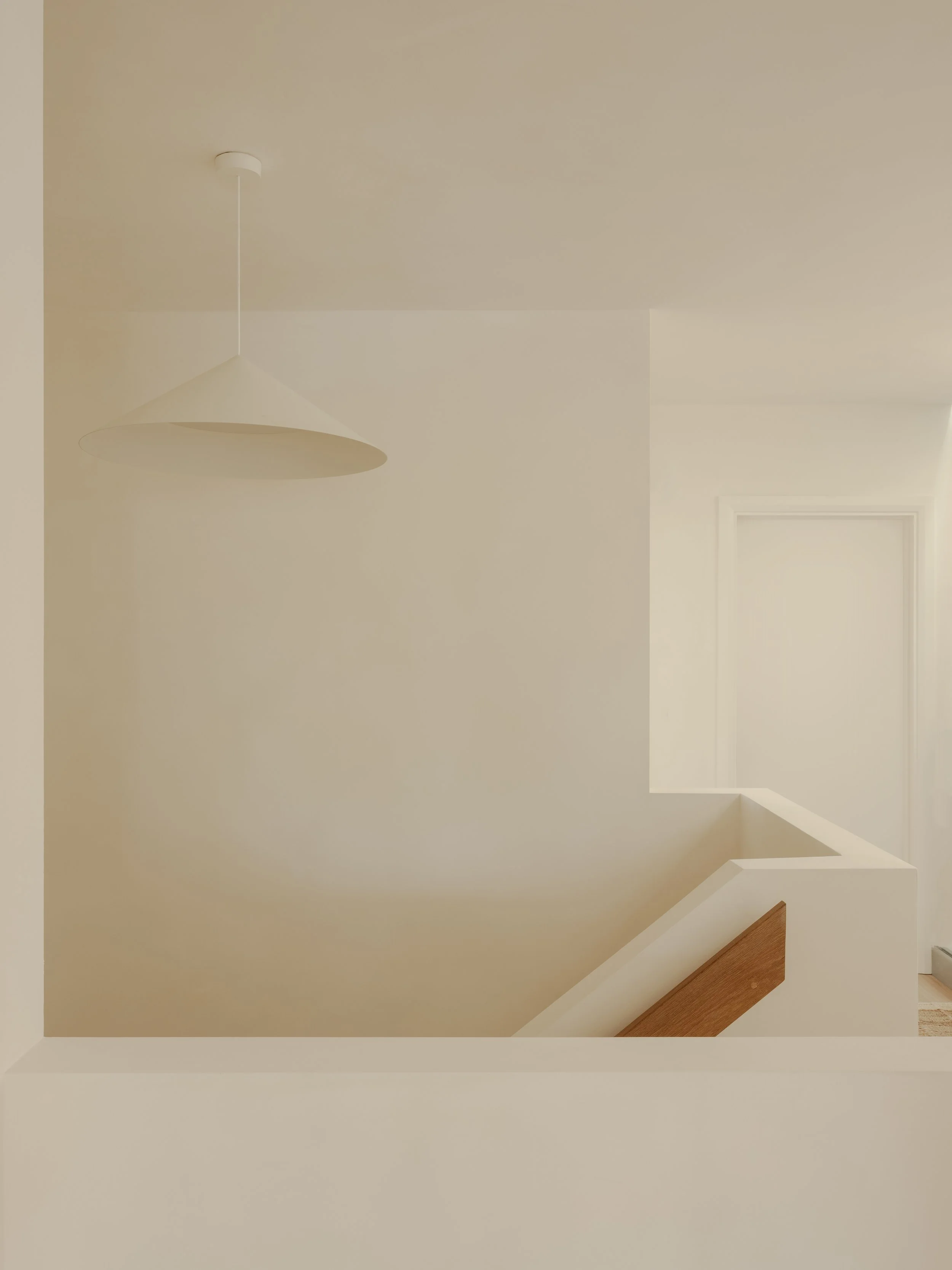 Minimalist interior with white walls, a ceiling light fixture, and a staircase with a wooden handrail.