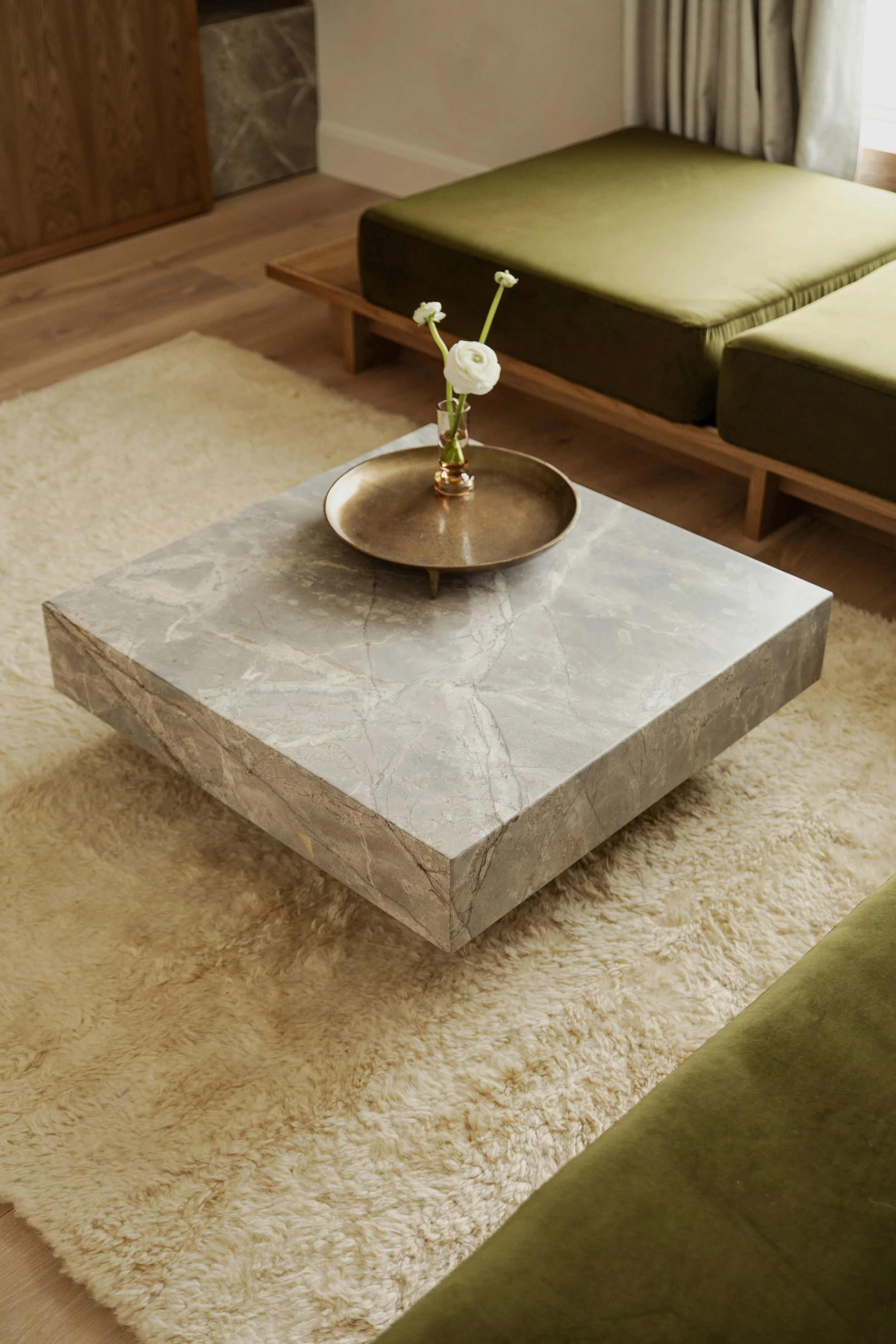 bespoke coffee table in grey fior di bosco marble with brass tray and vase with flower and cream high pile rug and green velvet bespoke sofa