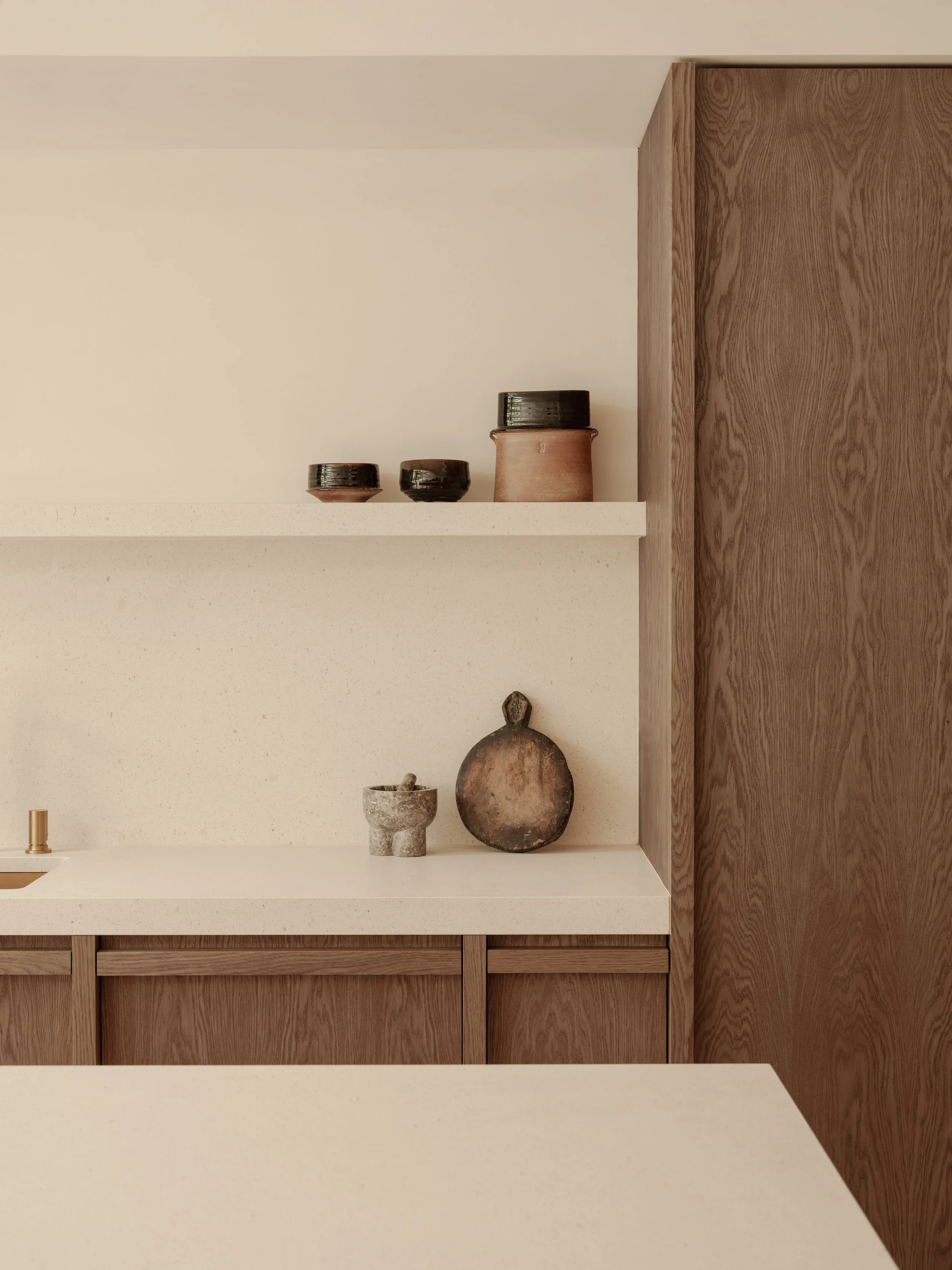 Minimalist kitchen shelf with ceramic bowls and a tray on white countertop against light wall and wooden cabinets.
