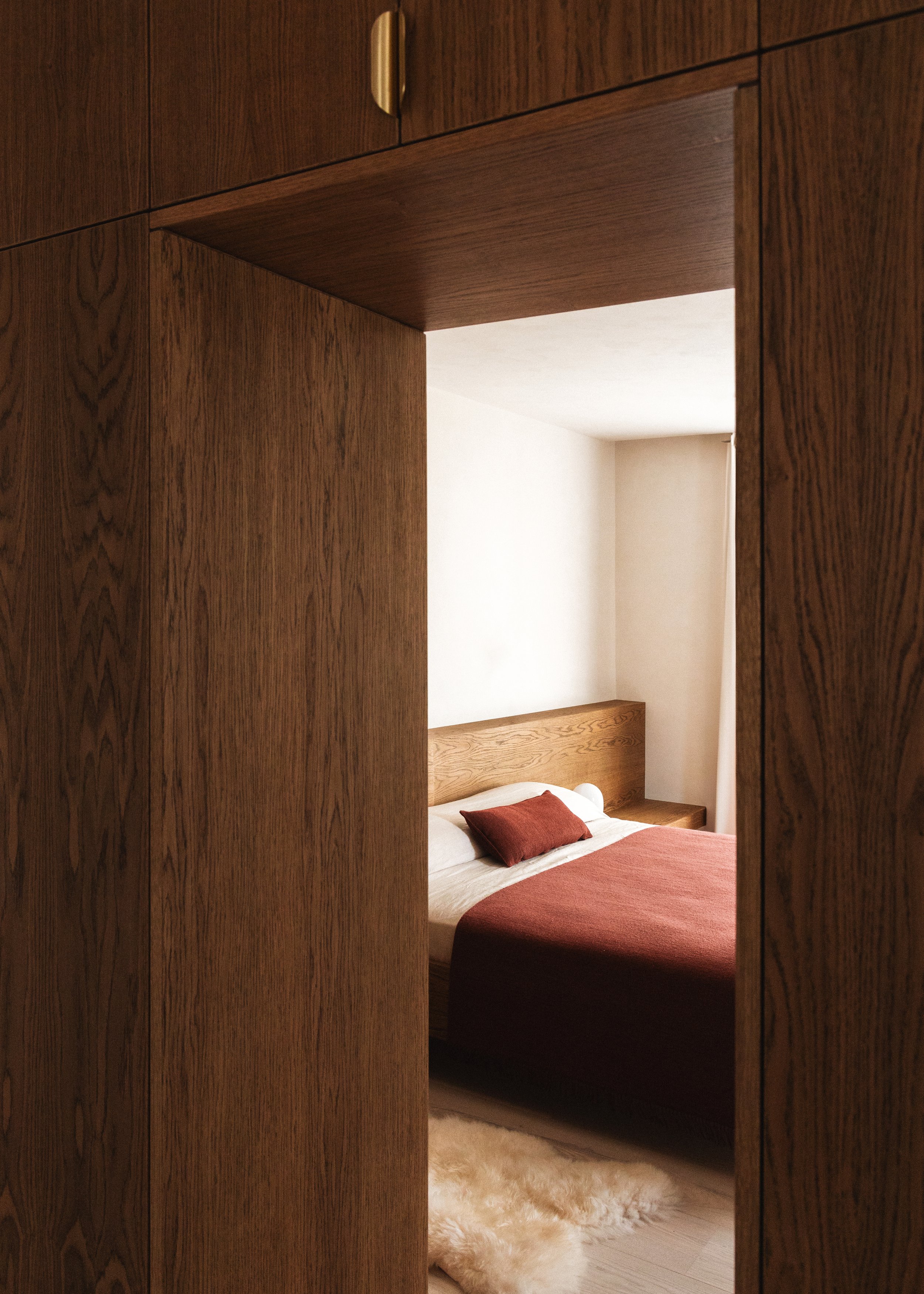 A doorway looking into a bedroom with a bed, wooden headboard, and matching side tables, with a plush beige rug on the floor.
