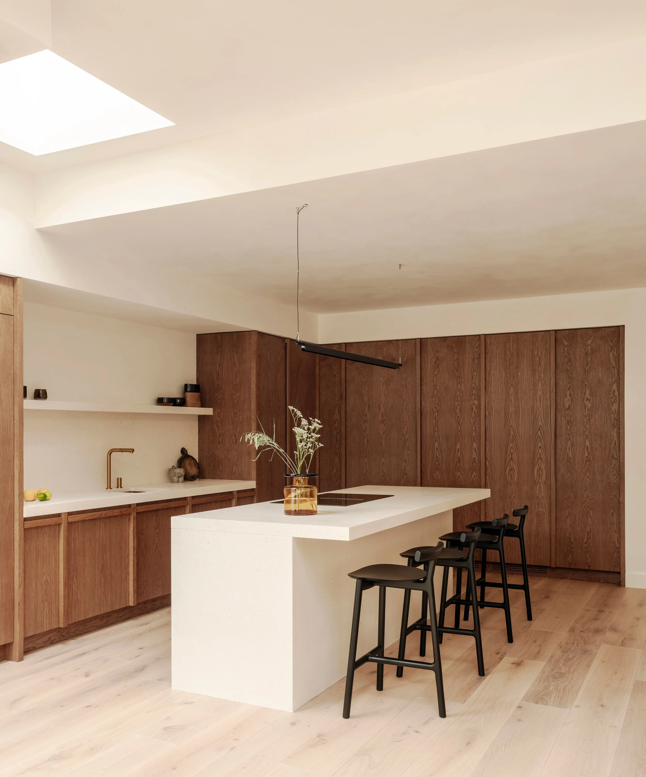 Modern kitchen with wooden cabinets, white island with a plant, and black bar stools.
