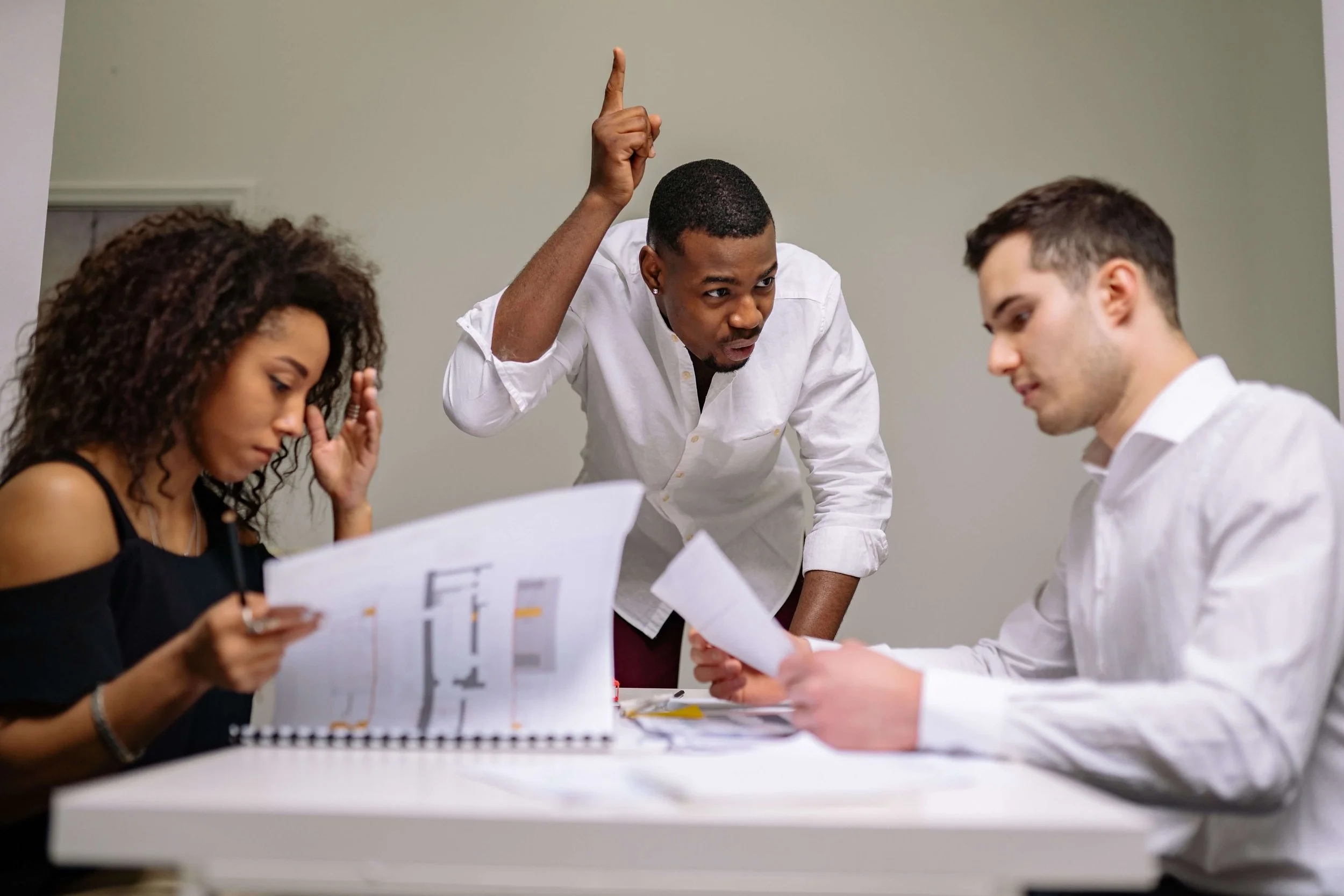 A man stands pointing upward while gesturing at a woman and another man who are reviewing paper. Family business consulting in Kansas City, MO helps families work through disagreements before they turn into shouting matches.