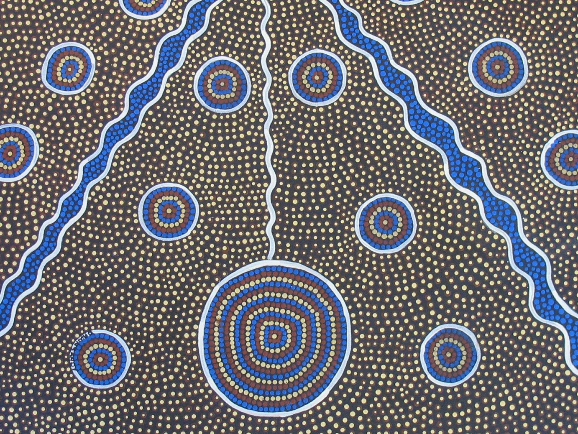Indigenous Australian dot painting with concentric circles, wavy lines, and dotted patterns in blue, brown, yellow, and white colors.