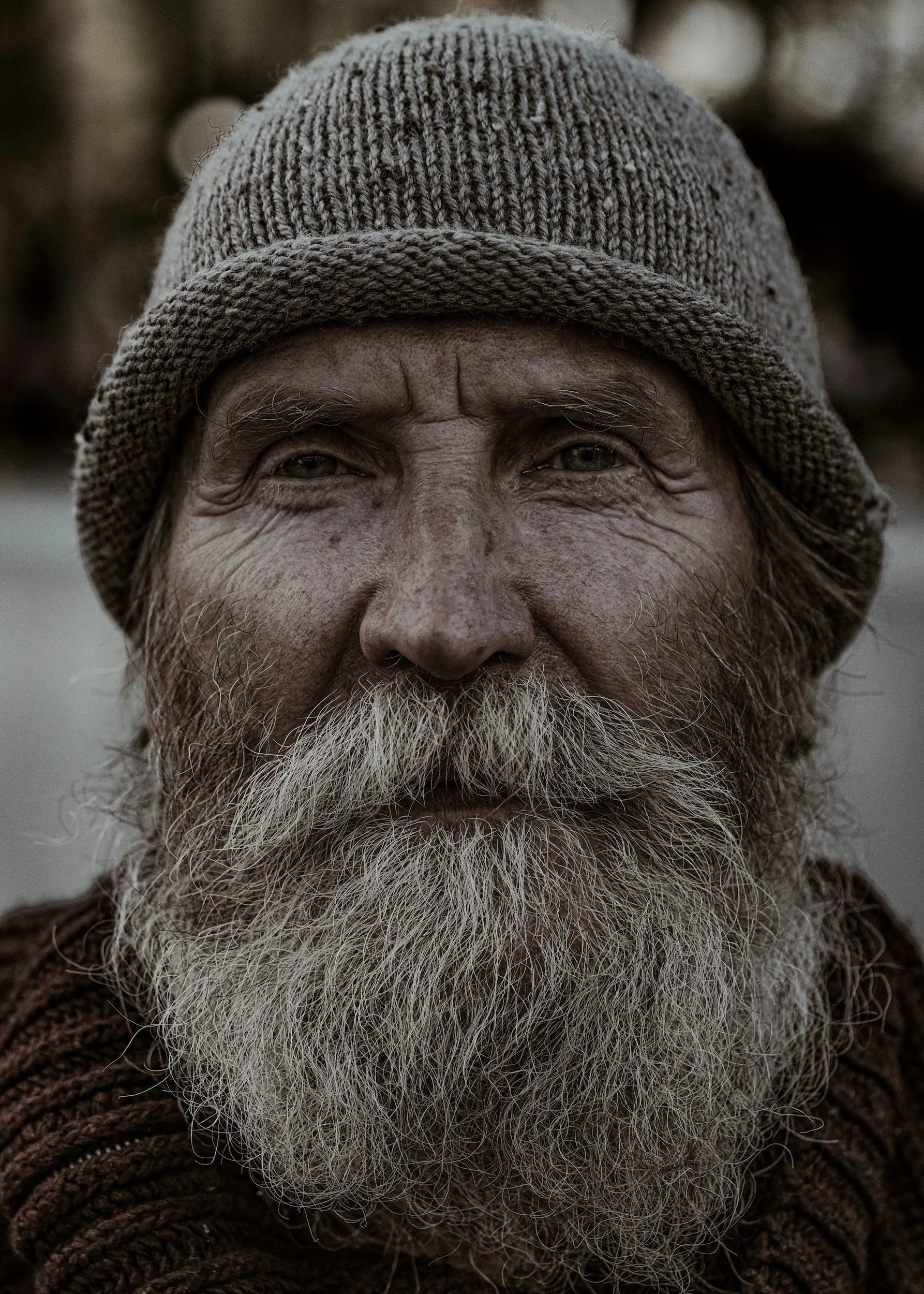 Close-up of an elderly man wearing a knit cap, with a full white beard and bushy eyebrows.