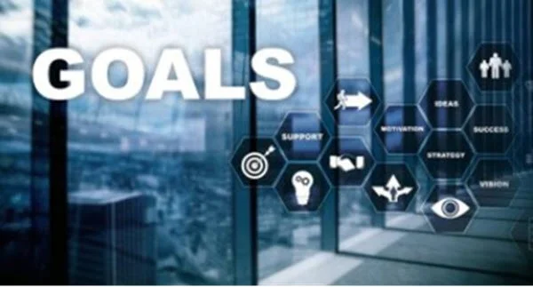 A modern office building with a large window showing a city skyline, featuring a graphic with the word 'GOALS' and various icons representing support, inspiration, strategy, vision, success, and targets.