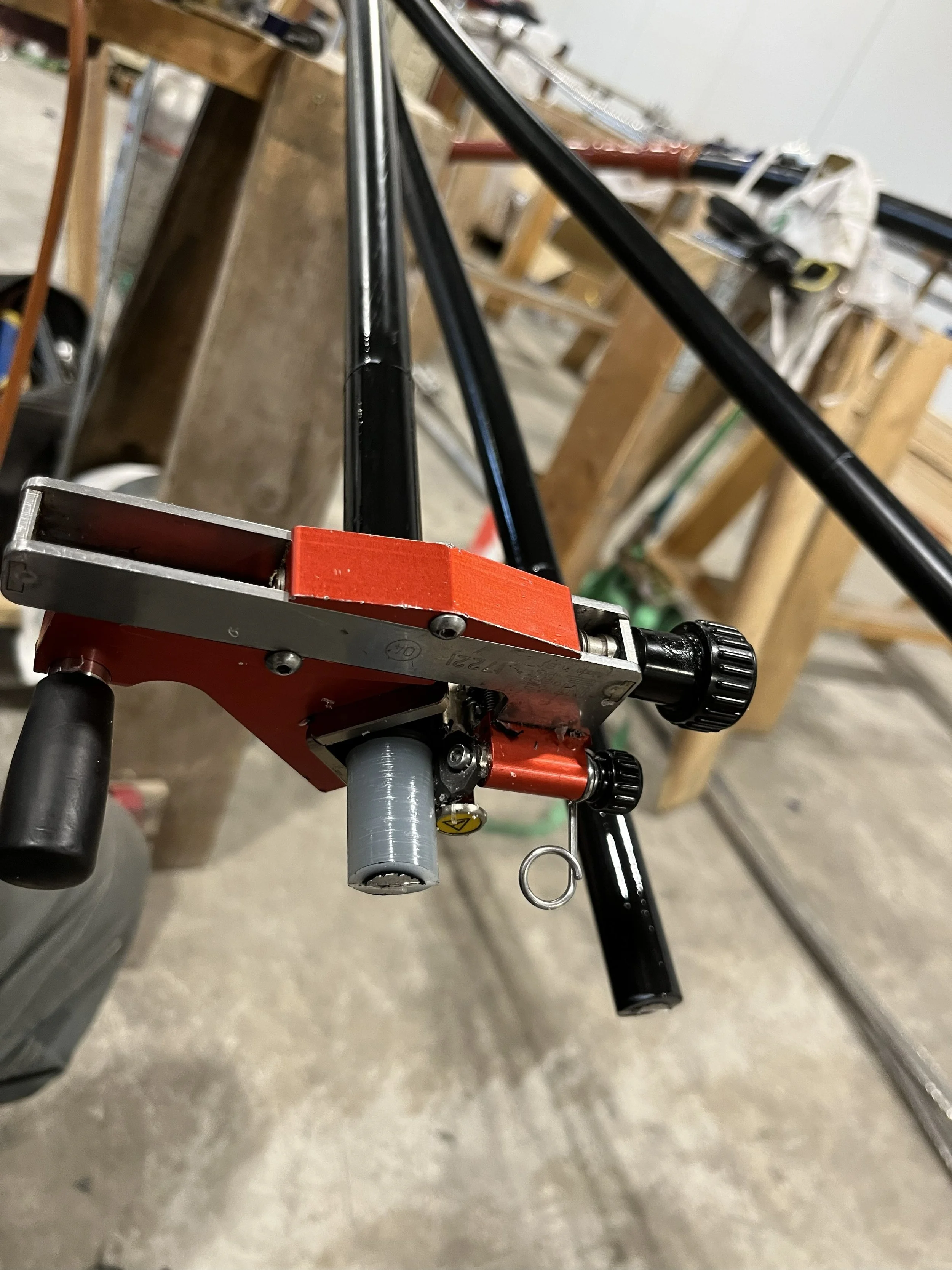 Close-up view of a workbench with black metal tubes, a red clamp, and various tools in the background.