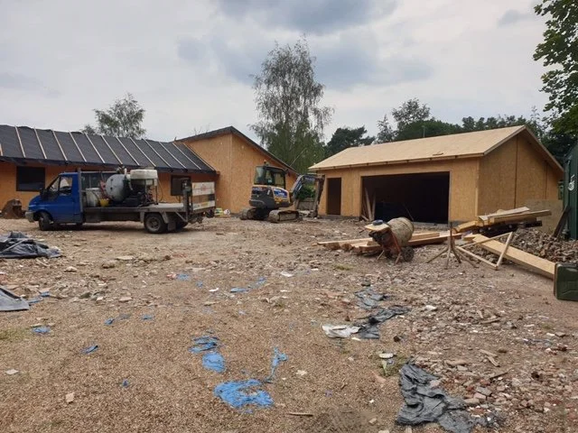 Construction site with two partially built wooden structures, construction vehicles, and scattered debris on the ground.