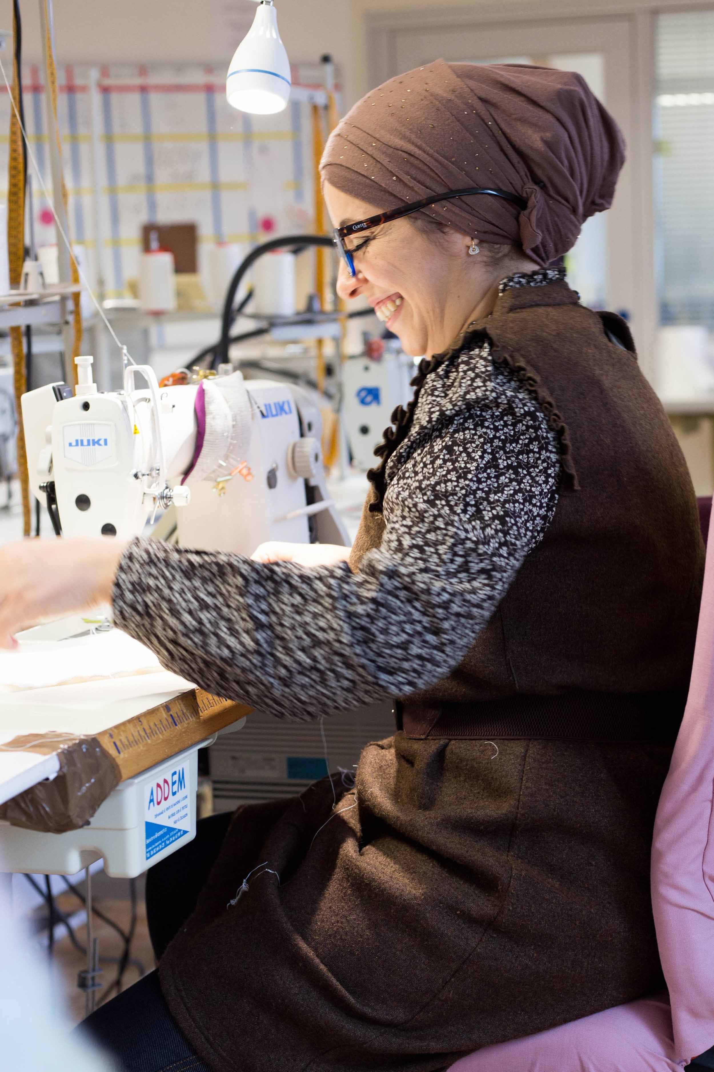 Une femme portant un foulard travaille sur une machine à coudre dans un atelier de couture.