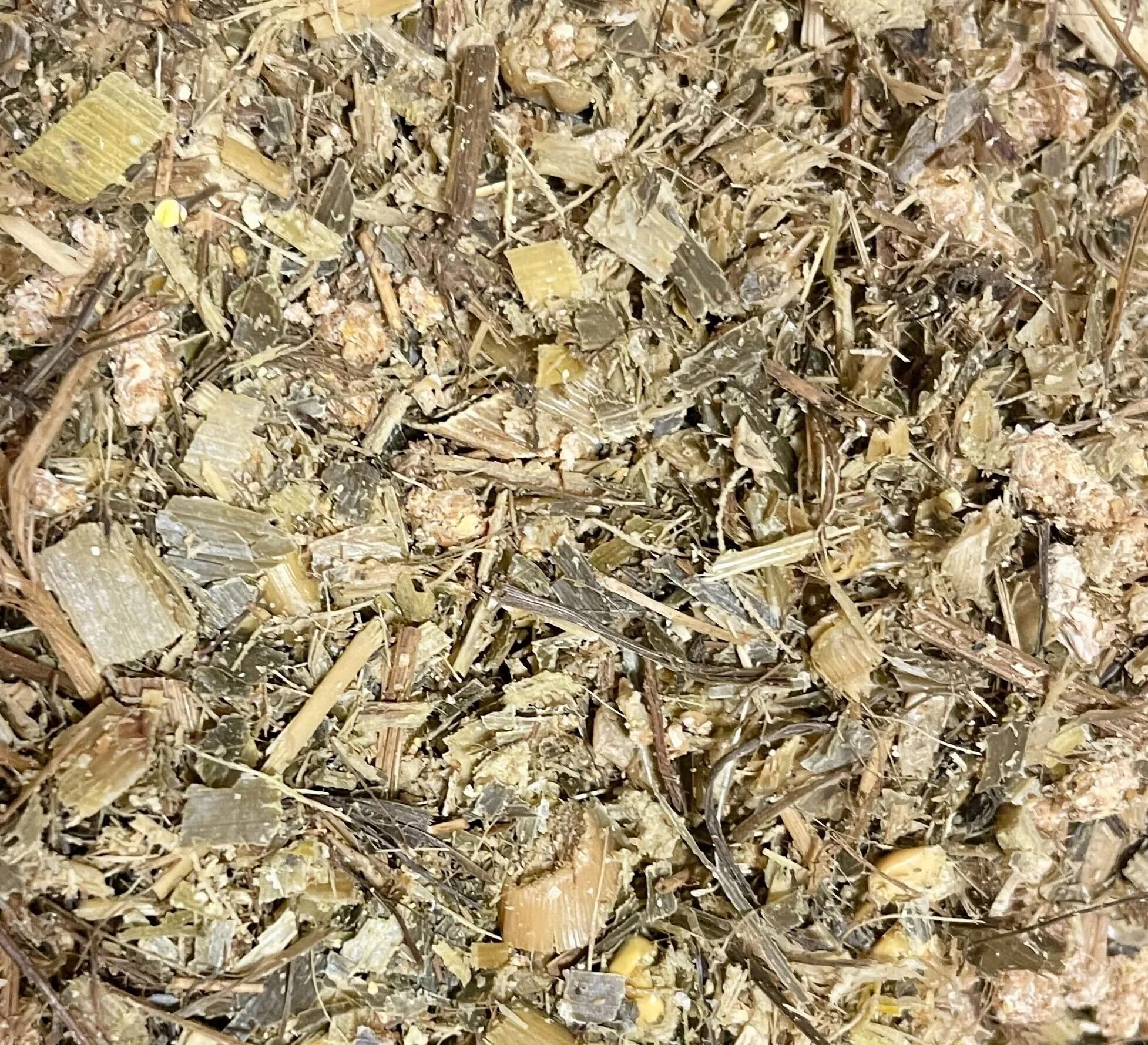 Close-up of a mixture of crushed vegetable scraps, including pieces of corn husks, stalks, and husks, used for composting or mulch.