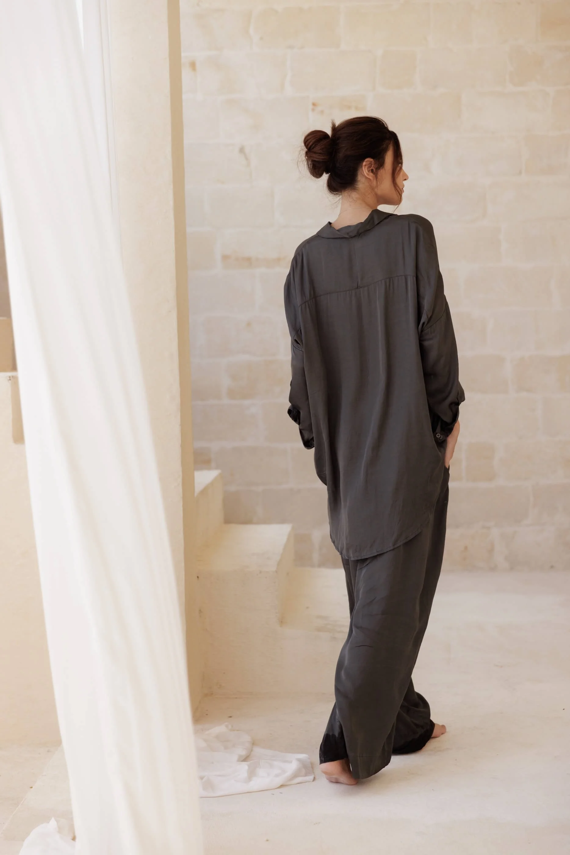 Rear editorial view highlighting the construction of the Lolita shirt in Dust Grey, showcasing the clean yoke division and the elongated, rounded back hem reaching near the knees.