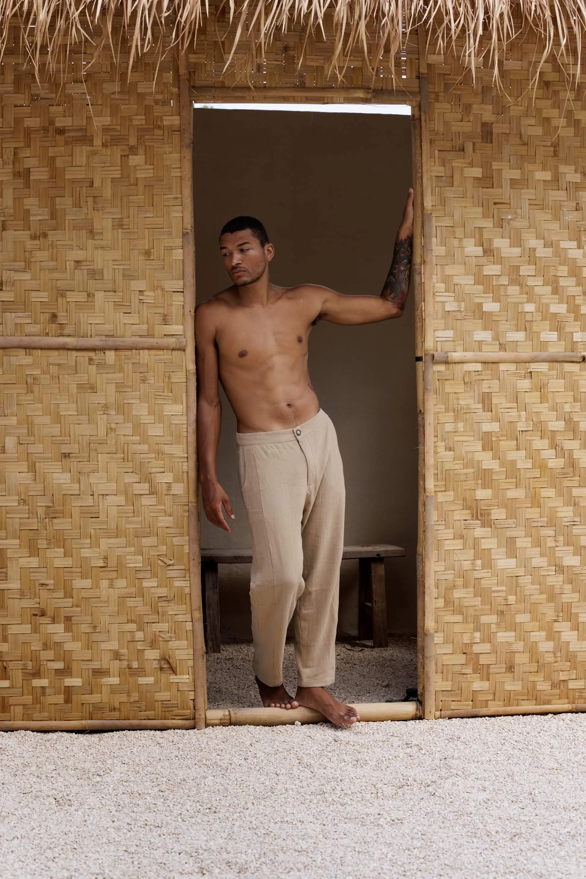 Full-length editorial lifestyle shot of the model wearing the Figueral structured cotton trousers in Sand Dune, emphasizing the natural fluid drape of the beige fabric.
