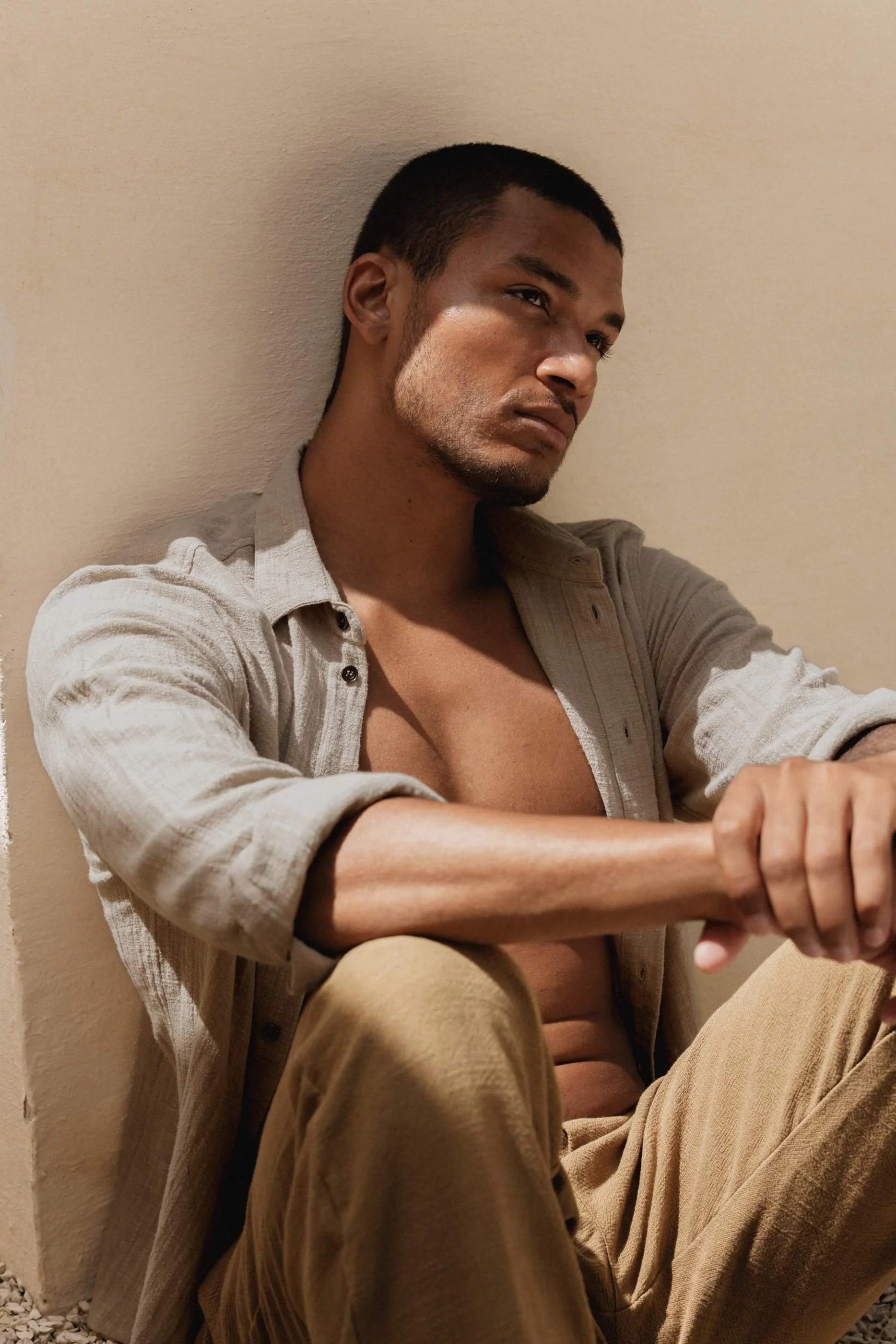 An editorial, introspective shot of the model sitting thoughtfully with the Mateu Sahara cotton gauze shirt styled open, capturing the raw, relaxed spirit of the collection.