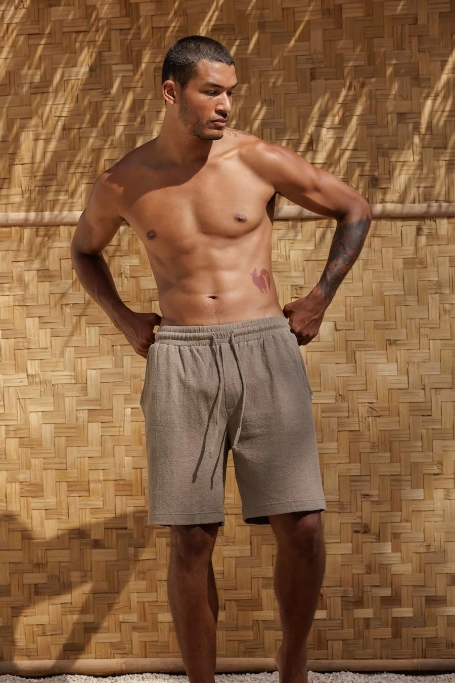 Man wearing NOUSA Renclì men's relaxed shorts in Ocean Fog green-grey linen-cotton jersey, front view showing elastic waistband.