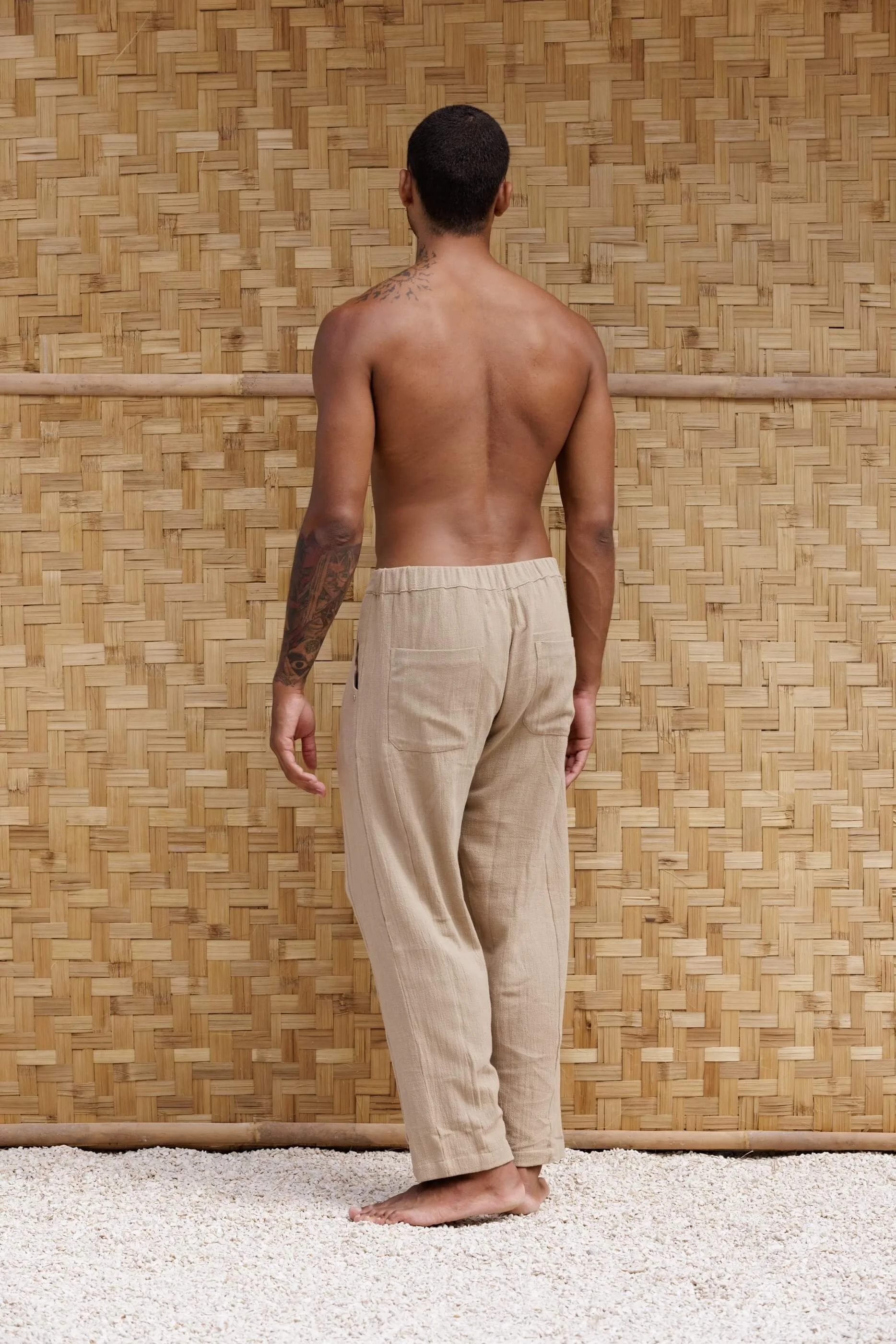 Three-quarter back view of the model wearing the Figueral Sand Dune trousers, showcasing the architectural barrel-shape fit and the comfortable elasticated back waistband.