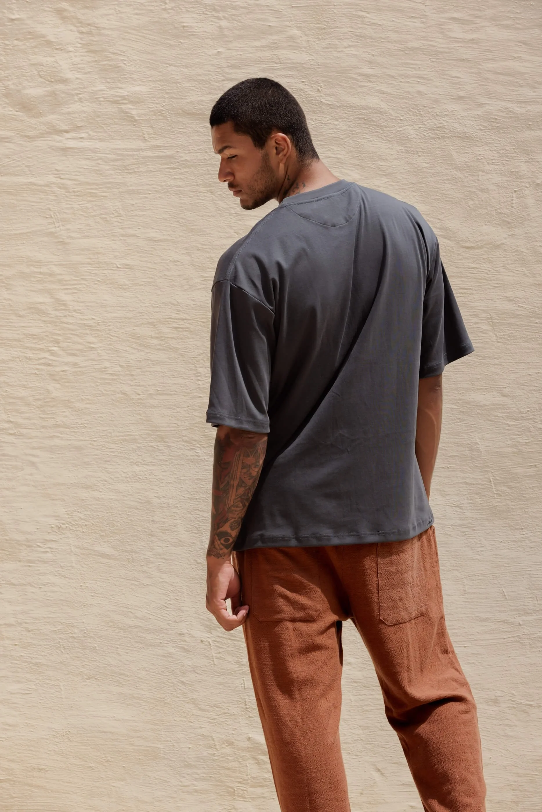 Three-quarter rear view of the model wearing the Gael oversized t-shirt in Metal, highlighting the relaxed boxy silhouette and the subtle hand-embroidered detail on the back hem.
