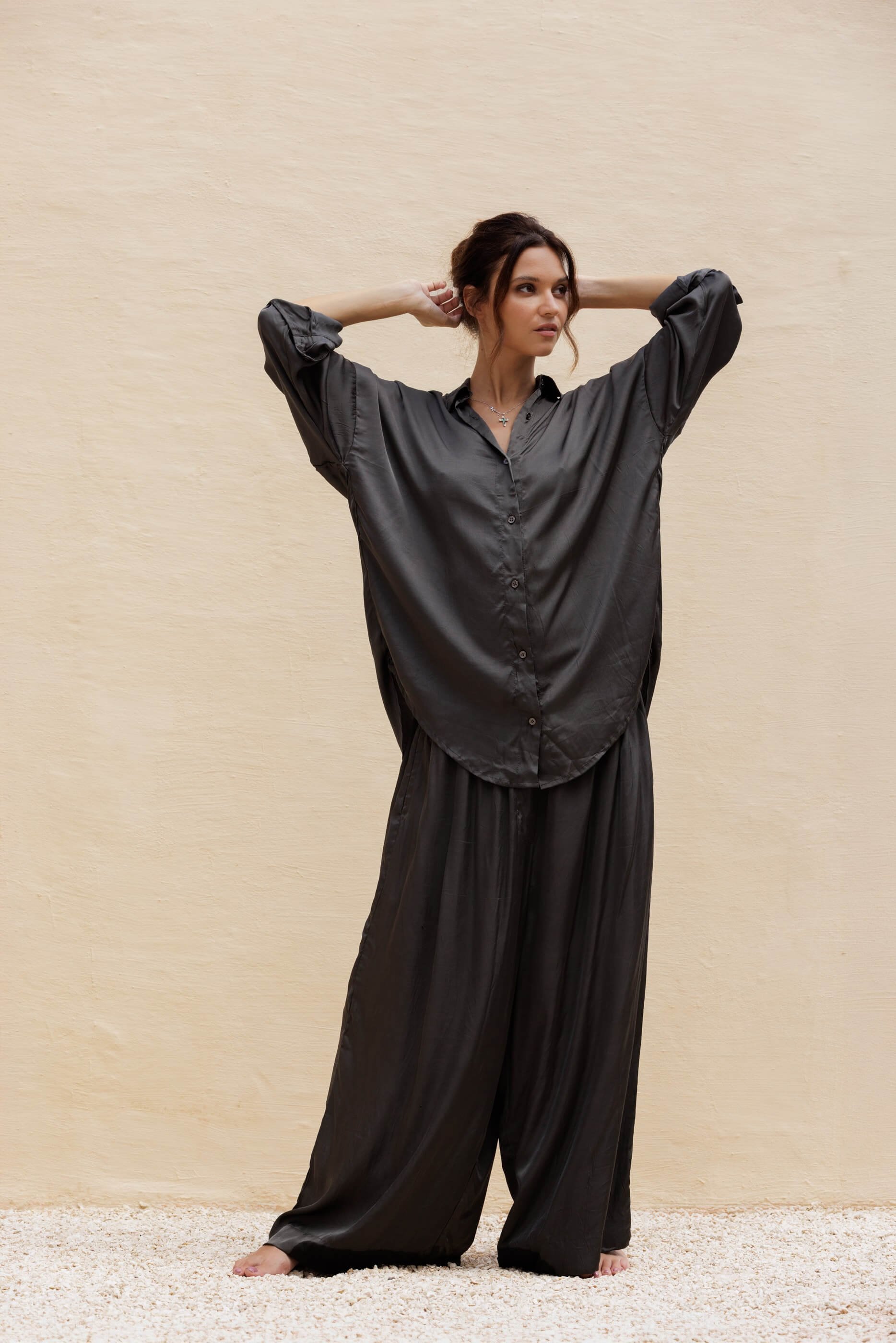 Full-length front view of the model standing straight in the unstructured Dust Grey Aguas satin pants, emphasizing their generous, relaxed fit and elegant everyday drape.