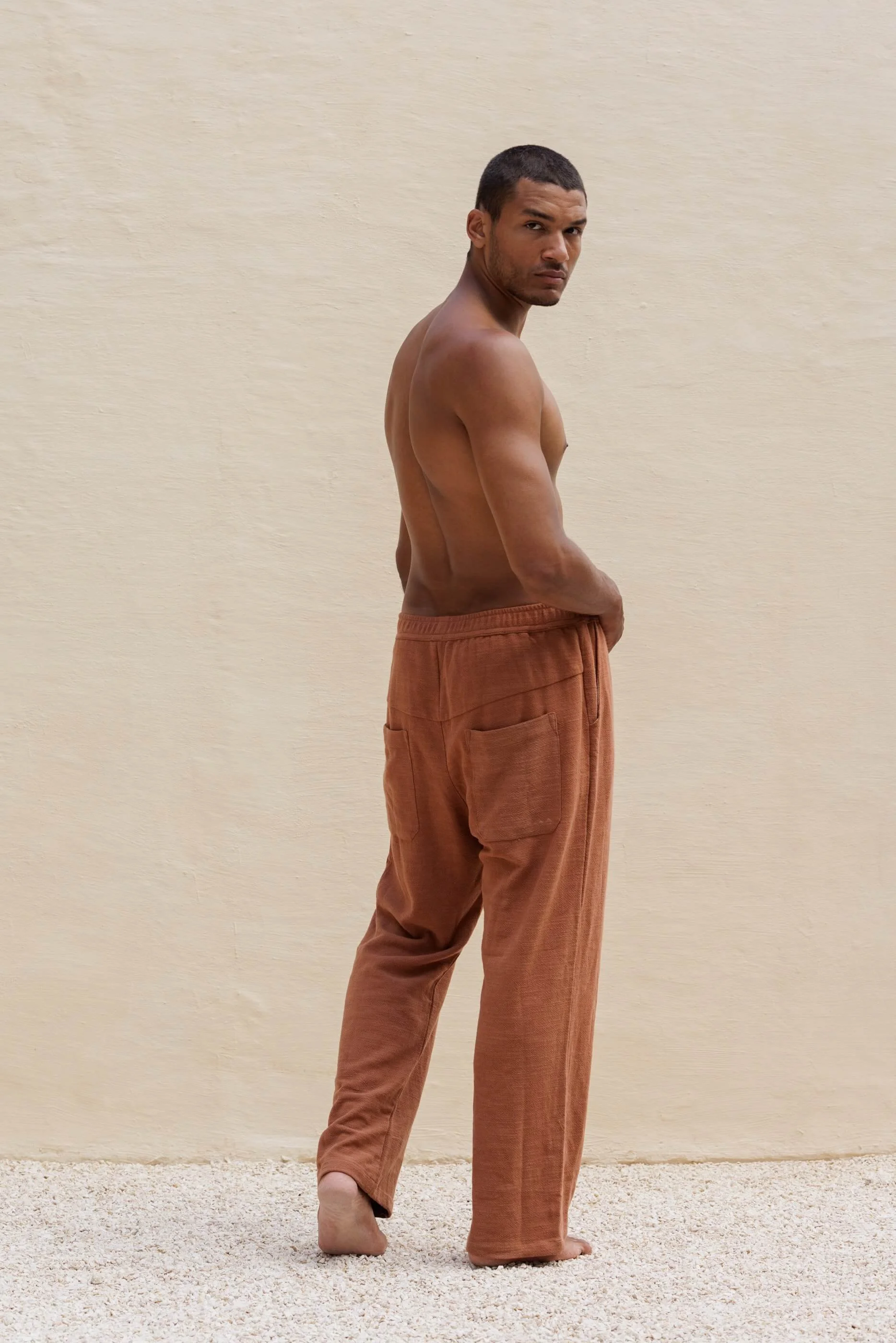 Full-length three-quarter back view of the model wearing the Benirras Terracotta trousers, emphasizing the relaxed tailored fit, elasticated waistband, and rear patch pockets.