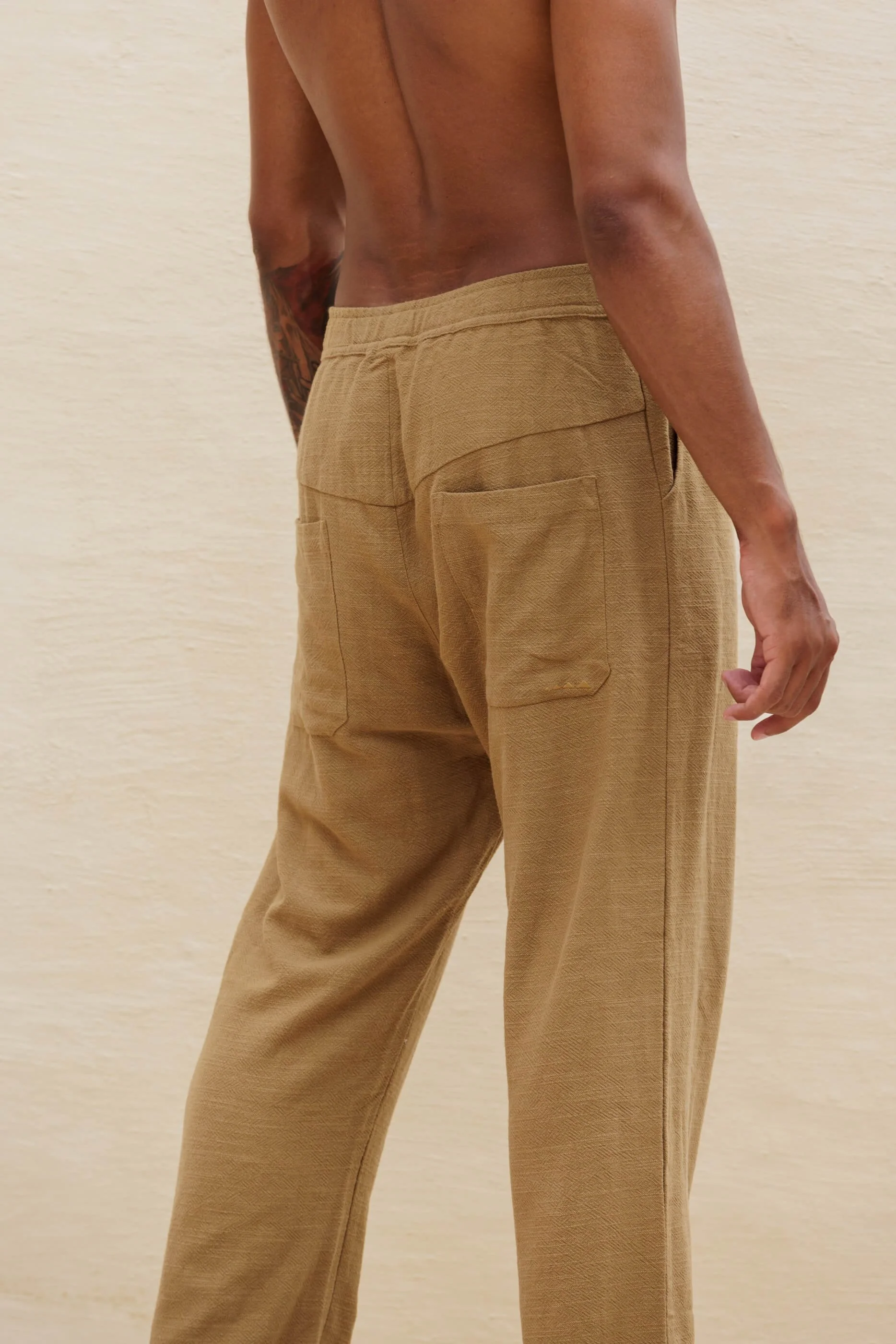 Close-up rear view of the Benirras Dust Olive Green trousers, highlighting the elasticated waistband, the distinct slanted seam dividing the back yoke, and the contemporary patch pocket.