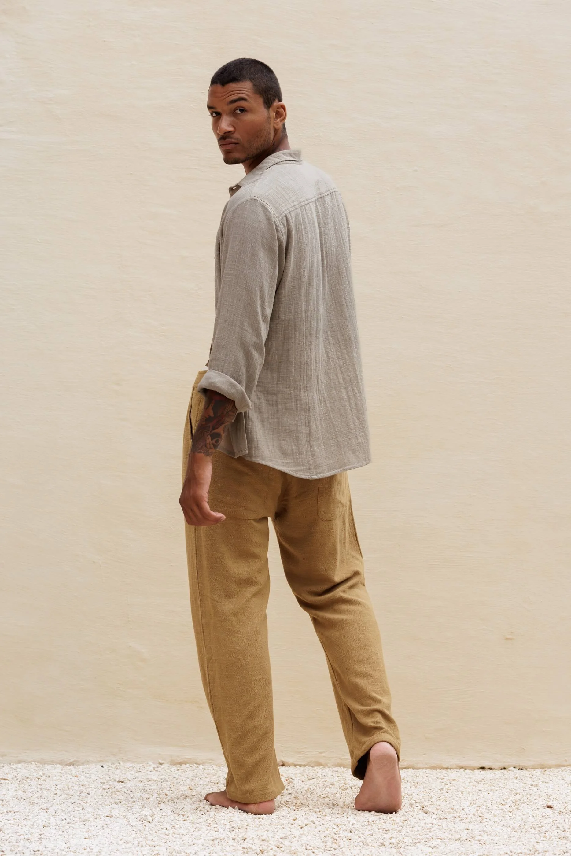 Full-length three-quarter back view of the model wearing the Benirras green trousers paired with the Mateu Sahara shirt, emphasizing the relaxed yet sophisticated tailored fit.