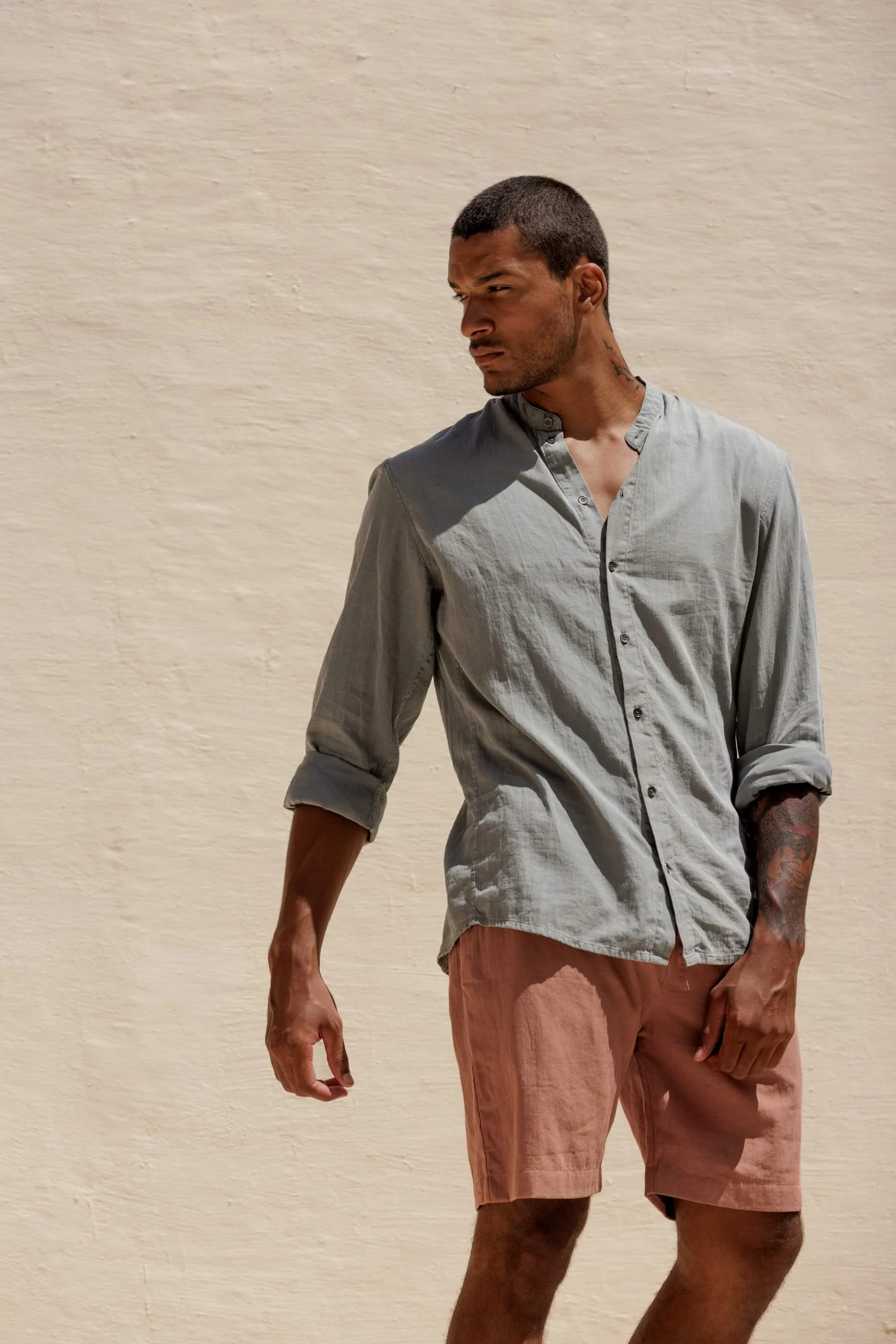 Three-quarter front view from the knee up of the terracotta Renclì shorts styled with the matching Jordi mandarin collar shirt in Sage Stone for a complete summer outfit.