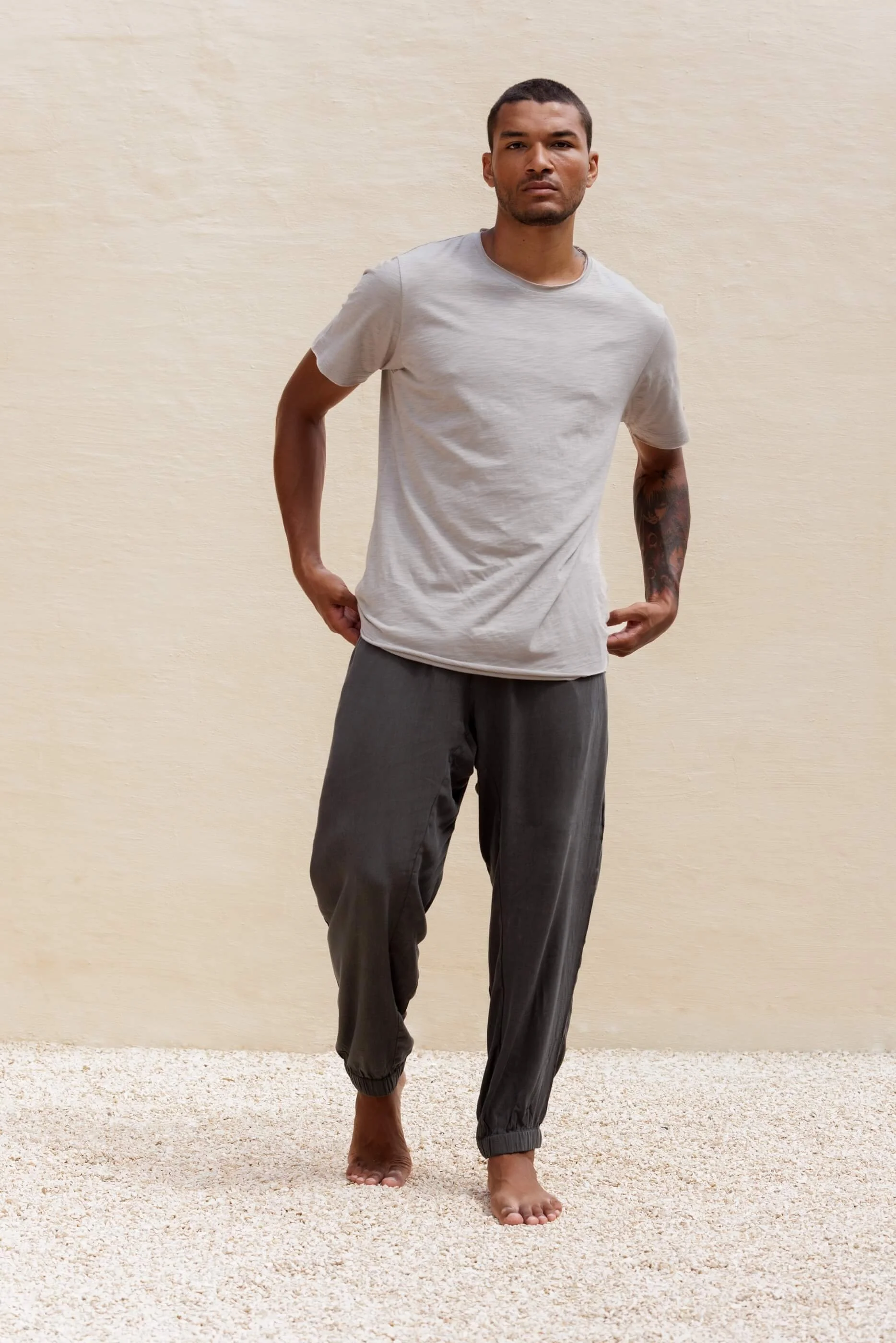 Full-length front view of a model wearing Gracio Dust Grey Tencel trousers paired with a simple t-shirt, showcasing the relaxed luxury leisurewear outfit.