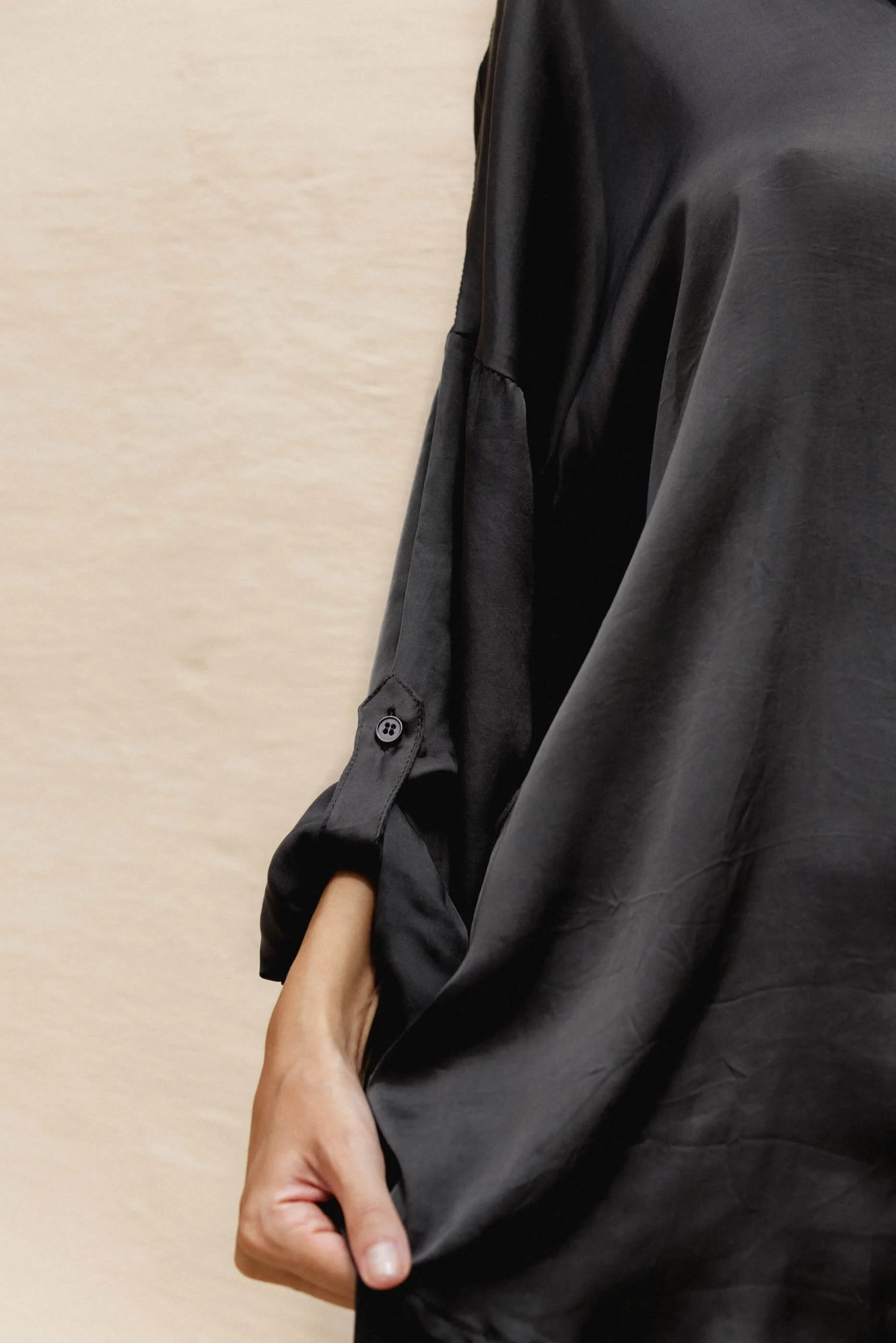 Close-up detail of the Dust Grey viscose satin fabric, highlighting the light reflections on the liquid texture, the rolled-up sleeve, and the delicate button construction.