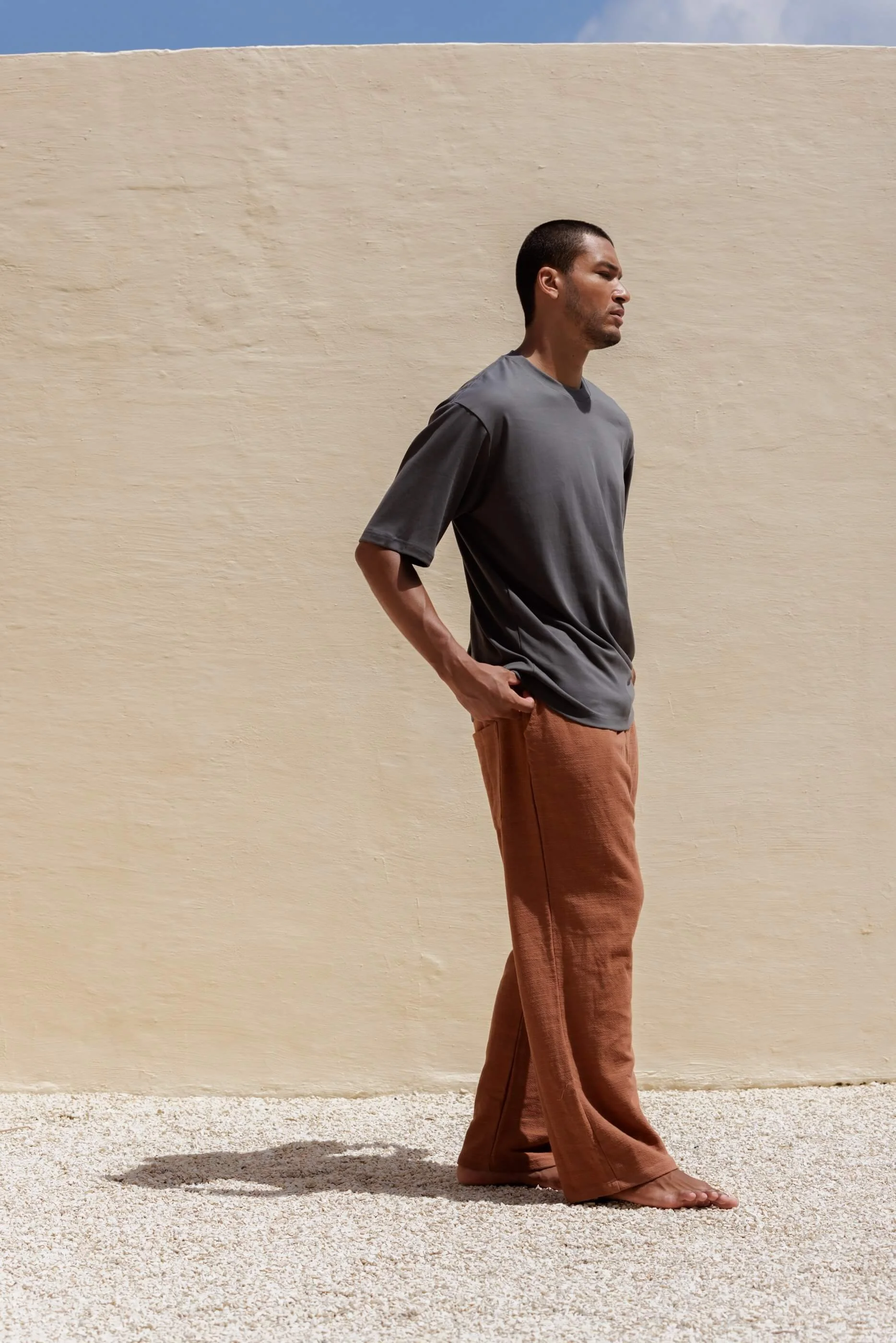 Full-length three-quarter front view of the model wearing the Terracotta linen-cotton pants paired with the Metal grey T-shirt, highlighting a contemporary, high-end lifestyle outfit.