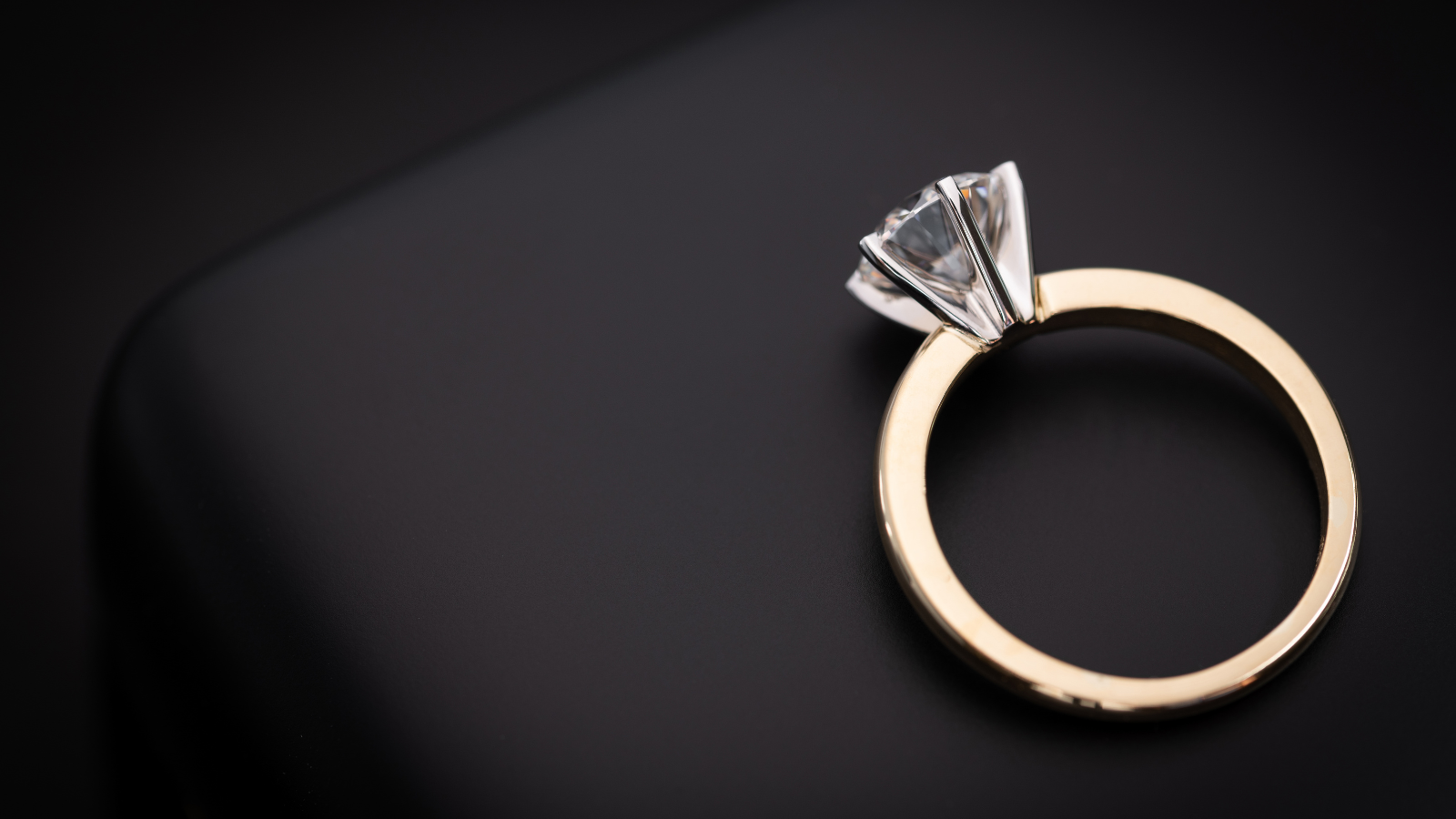 A gold ring with a large clear gemstone on a dark background