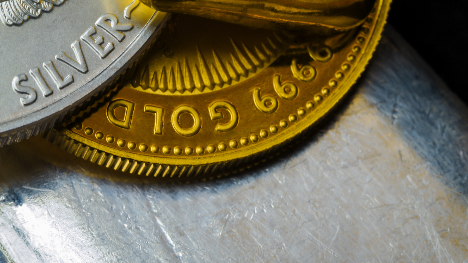 Close-up of stacked silver and gold coins, with the gold coin displaying the words 'GOLD' and the silver coin showing 'SILVER'.