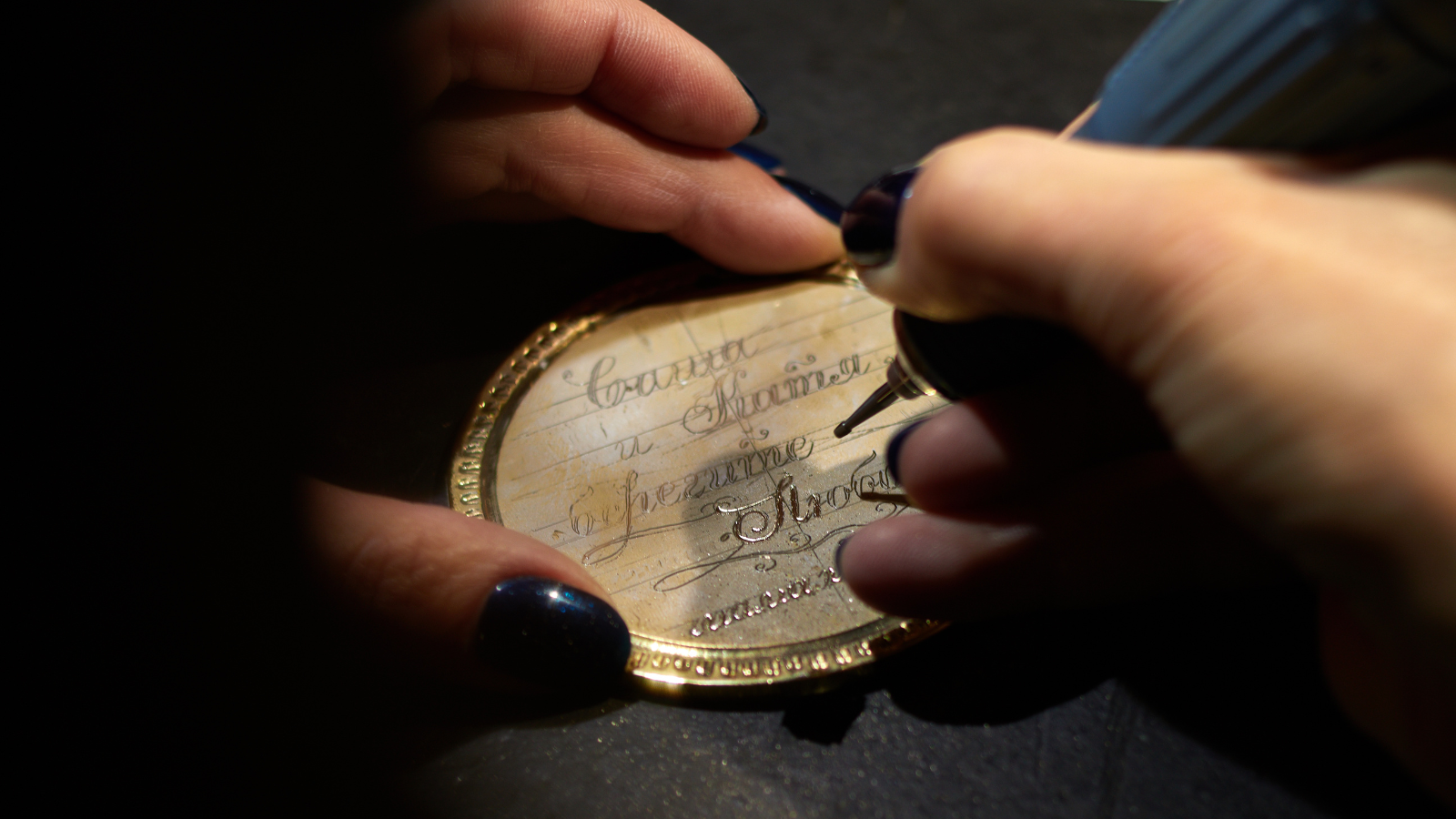 Person writes in cursive on a gold-colored metal case with a black pen, holding the case with both hands.