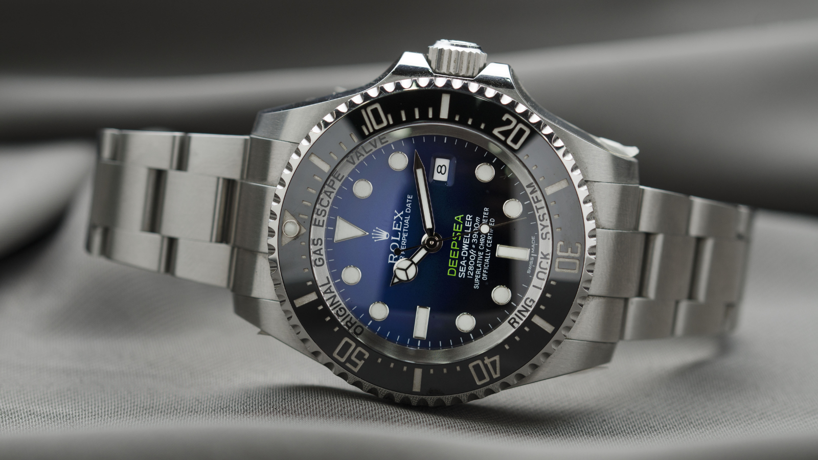 Close-up of a stainless steel Rolex Deepsea Sea-Dweller watch with a blue dial, black bezel, and a bracelet, resting on a gray surface.