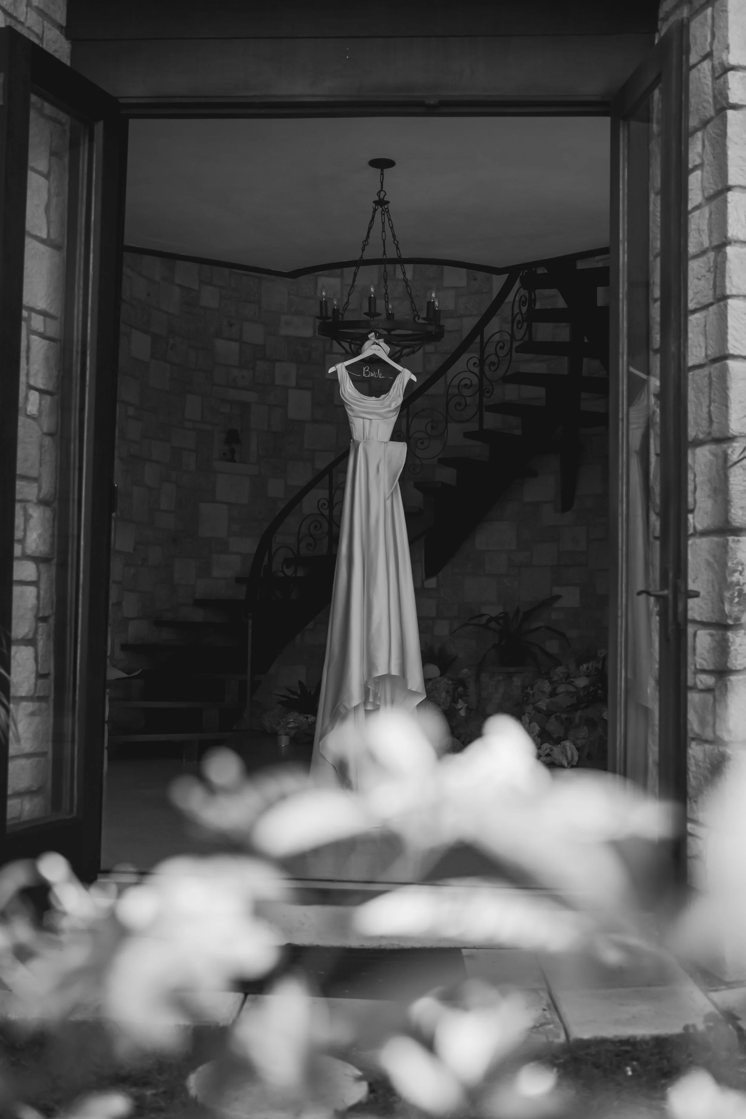 A dress hanging on a hanger in the doorway of a house, with a staircase and chandelier visible in the background.