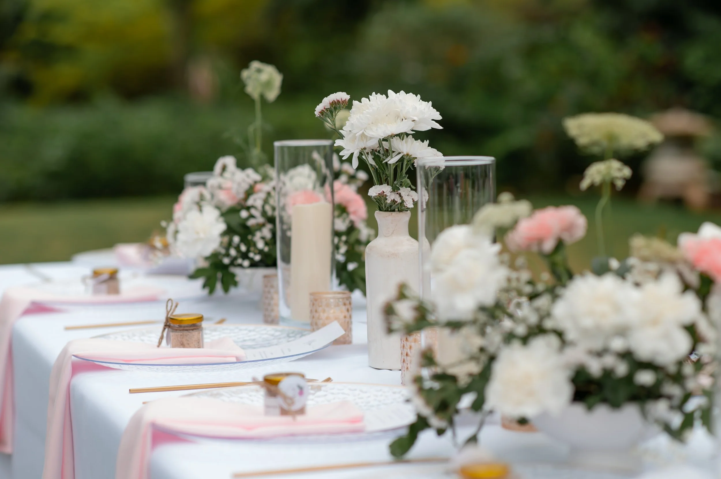 White flowers in vases and candles on a decorated outdoor table for a special event or celebration.