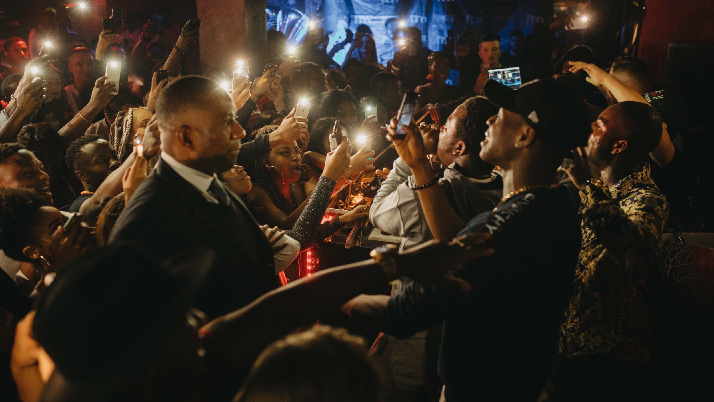 Menschenmenge bei einem Konzert oder Event, viele halten Smartphones hoch, um Fotos oder Videos zu machen, im Hintergrund bunte Lichter.
