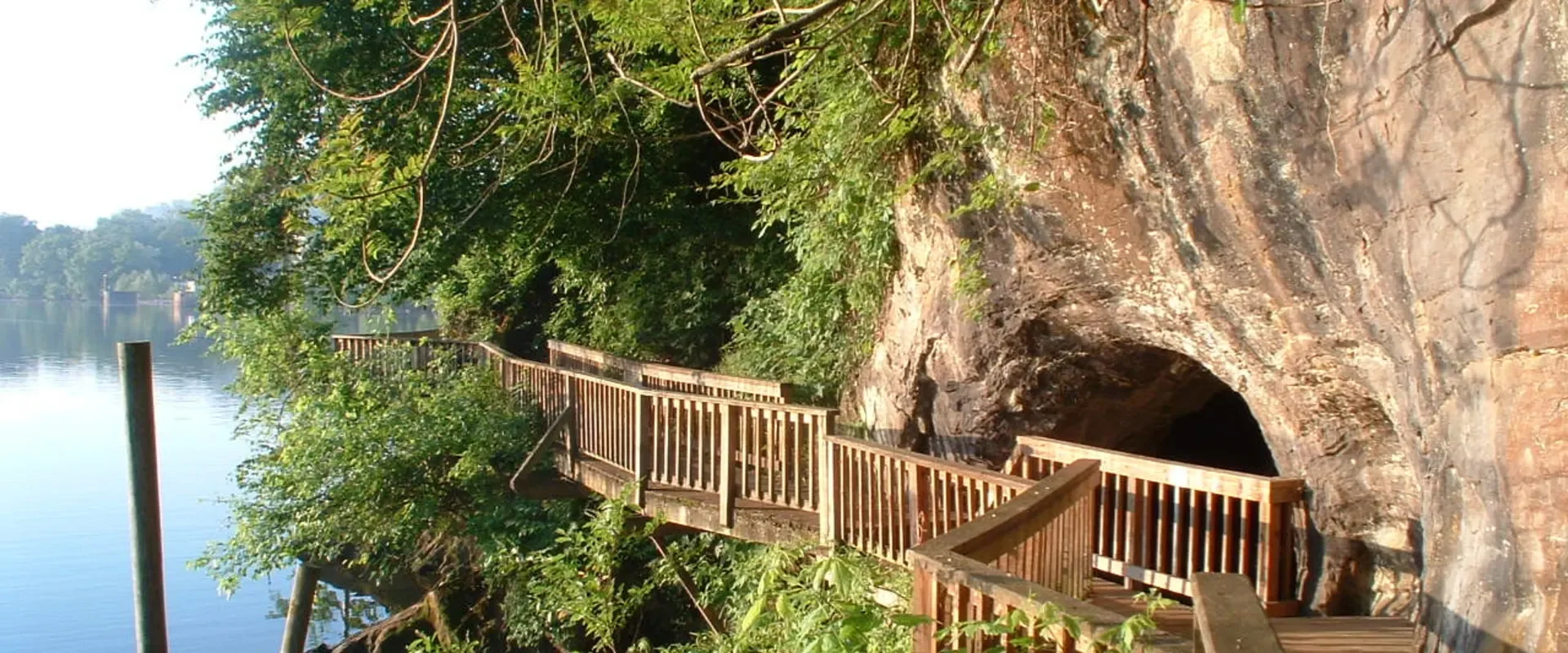 Wooden staircase leading into a rocky cave area near a lake, surrounded by green trees and foliage.