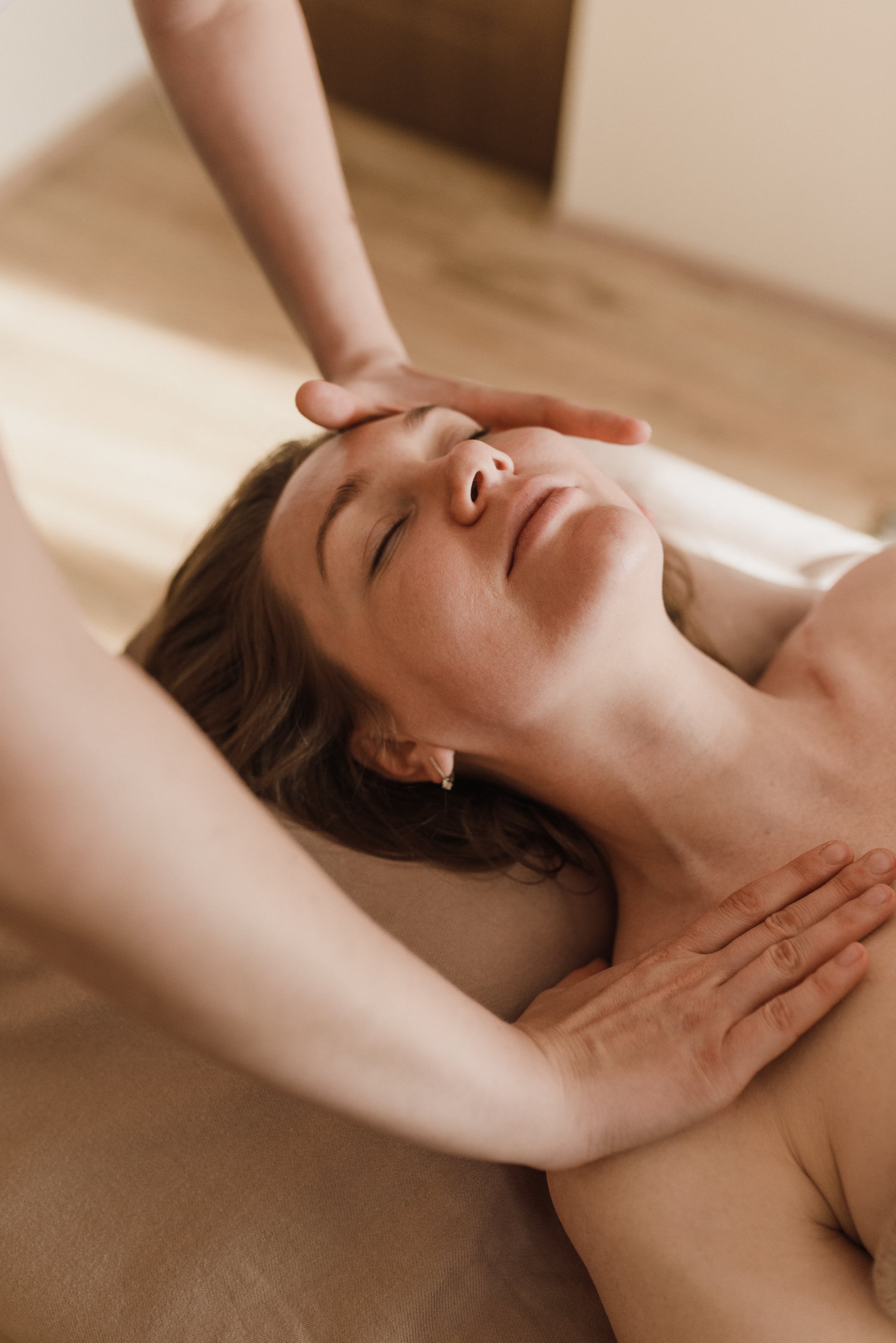 Woman lies on massage table face up. She is only visible from the neck up. A therapist's hands are place on the woman's collarbone and head, stretching the neck.