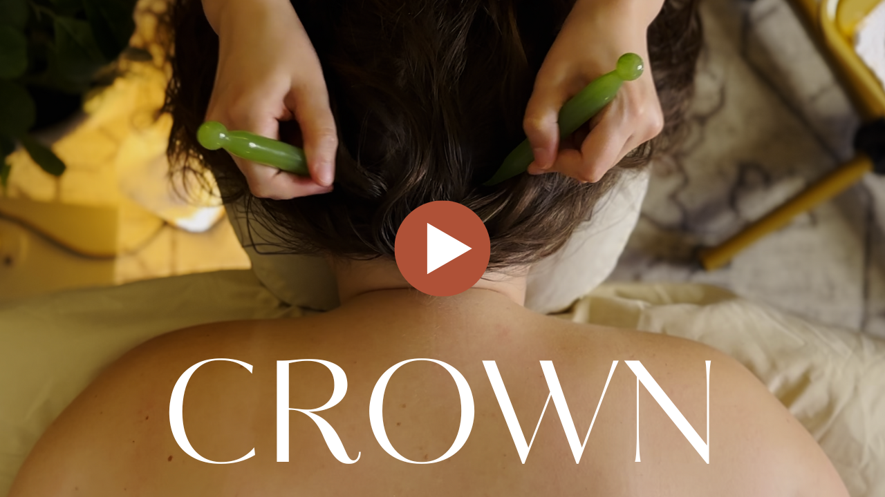 A top-down view of a person lying on a massage table. Acupressure pens are used by a therapist in either hand to massage the scalp.