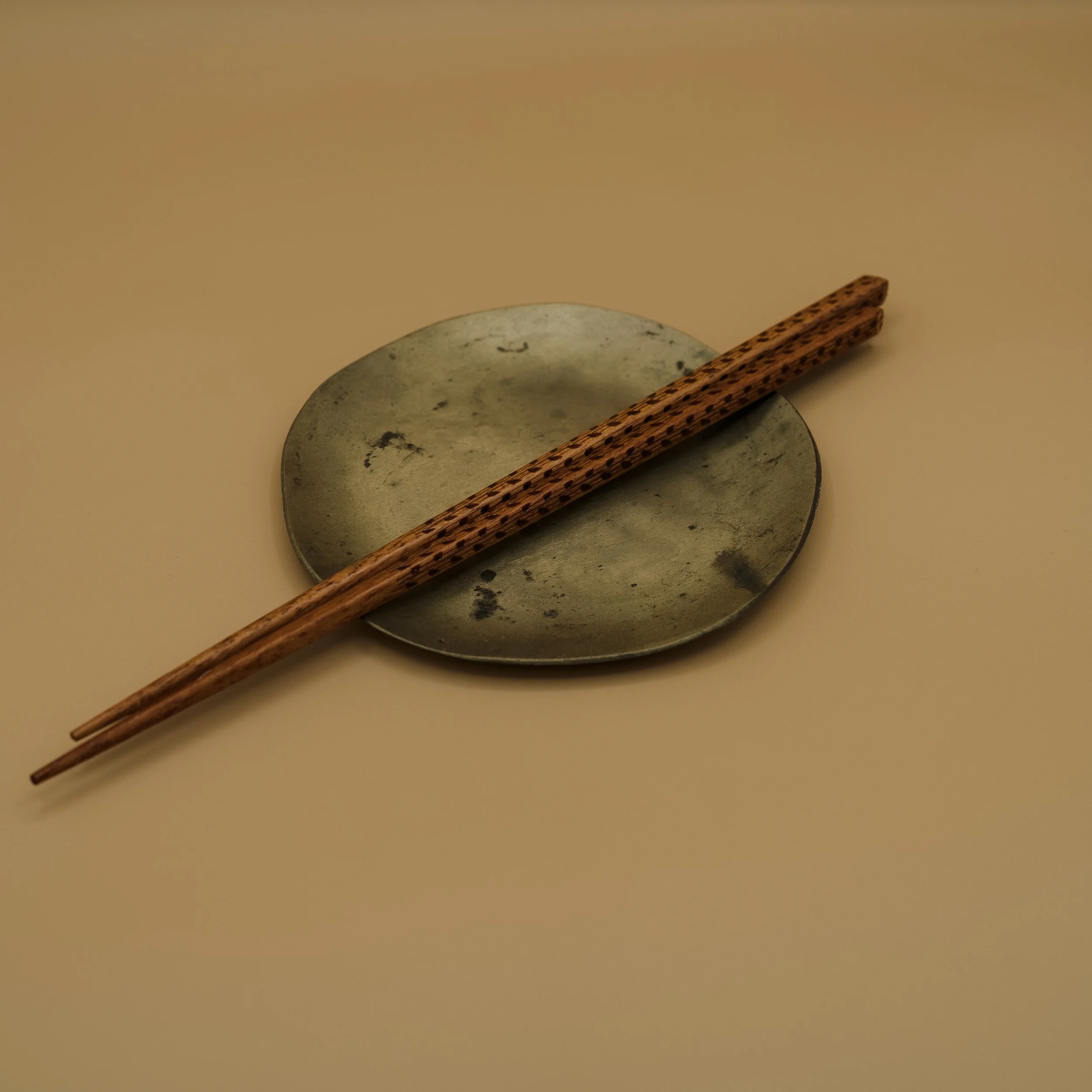 A pair of wooden chopsticks resting on a round, grey metal dish on a beige surface.