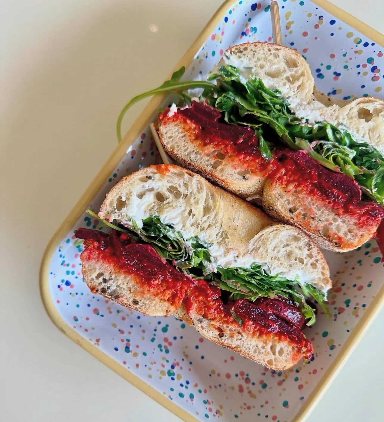 A plate with three small sandwiches with sliced bread, green leafy vegetables, and red sauce or spread, placed on a decorated tray.