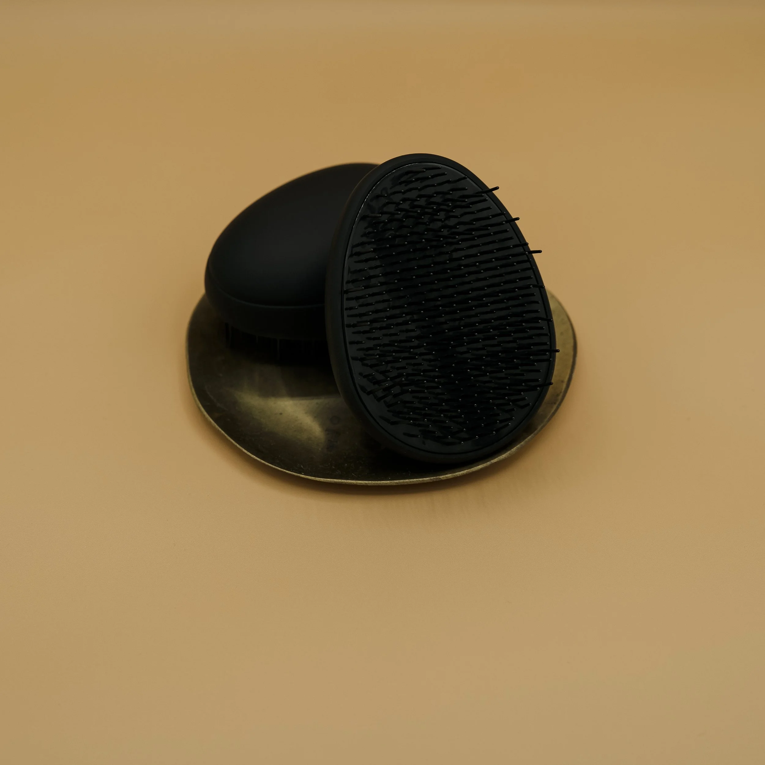 Black hairbrush with a rounded black case on a gold-colored surface