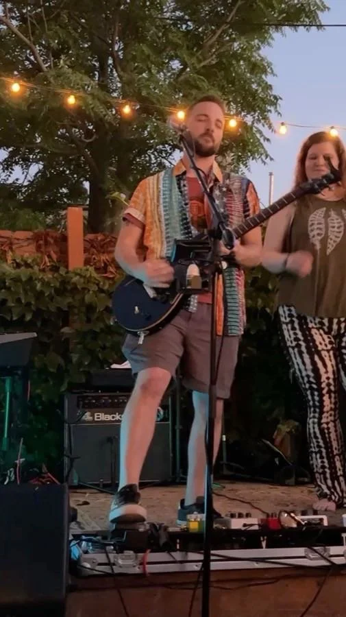 A guitarist and a singer performing outdoors with string lights.