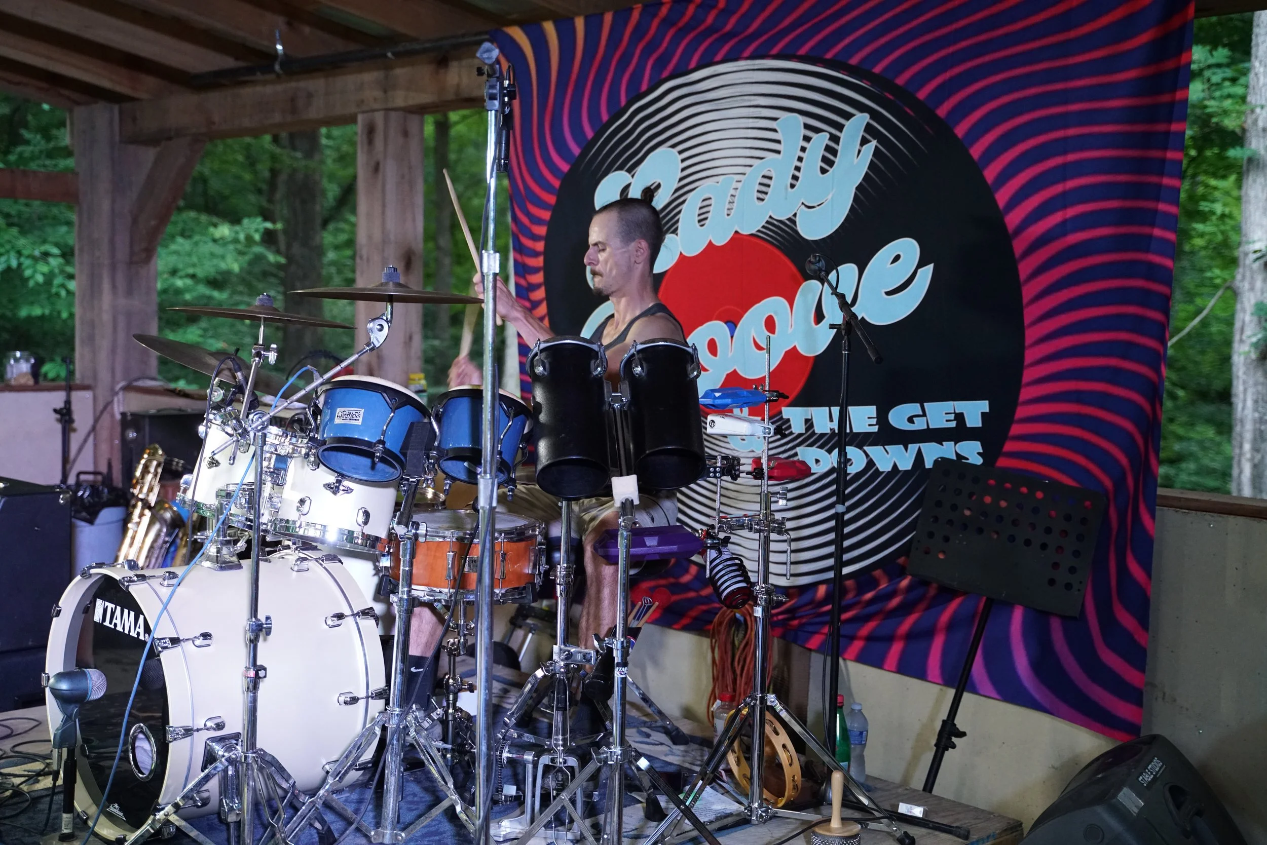 Drummer performing on stage with a white drum set in front of a colorful backdrop reading 'Lady Groove and the Get Downs.'